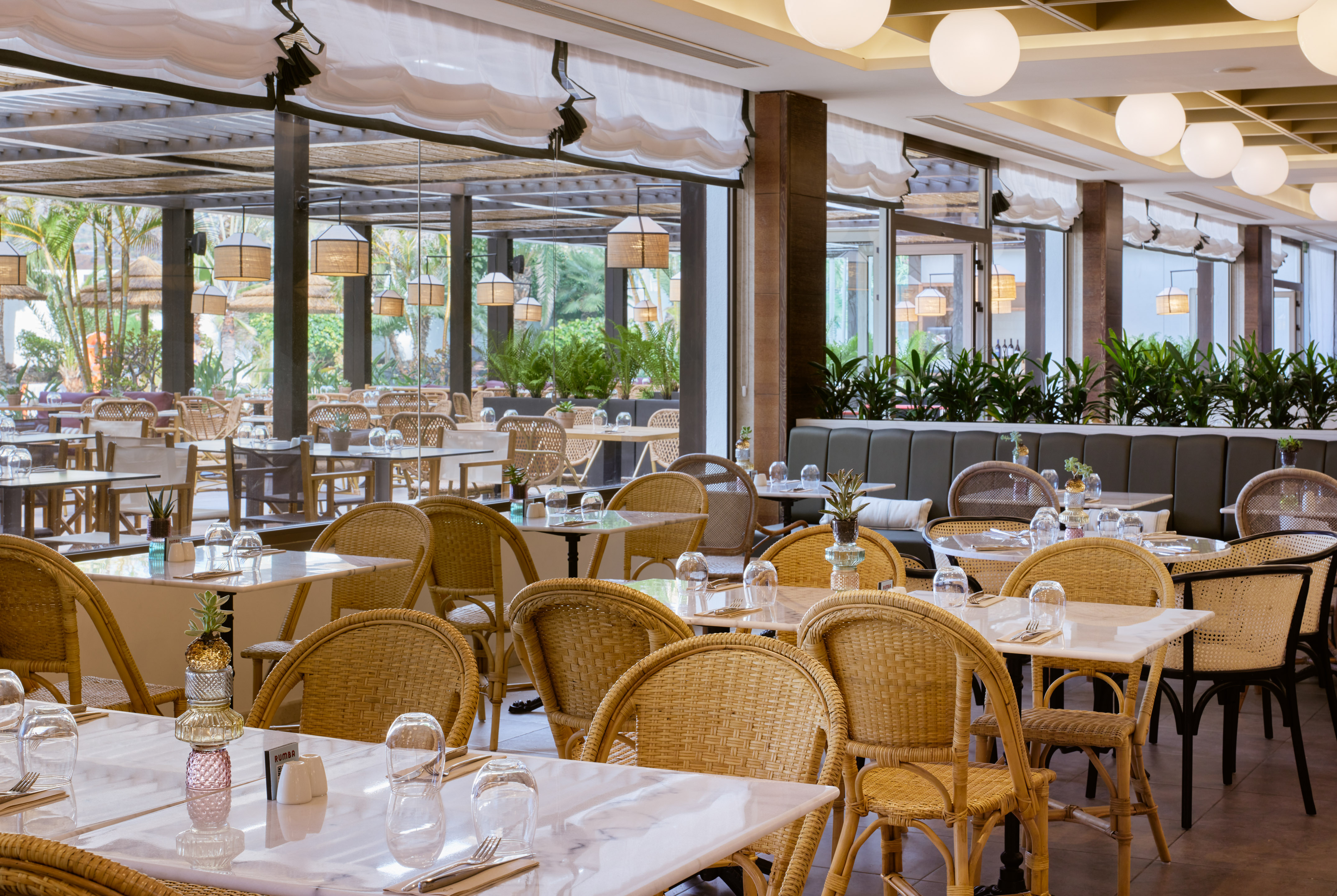 Bright resort restaurant with rattan chairs, marble tables, tropical setting.