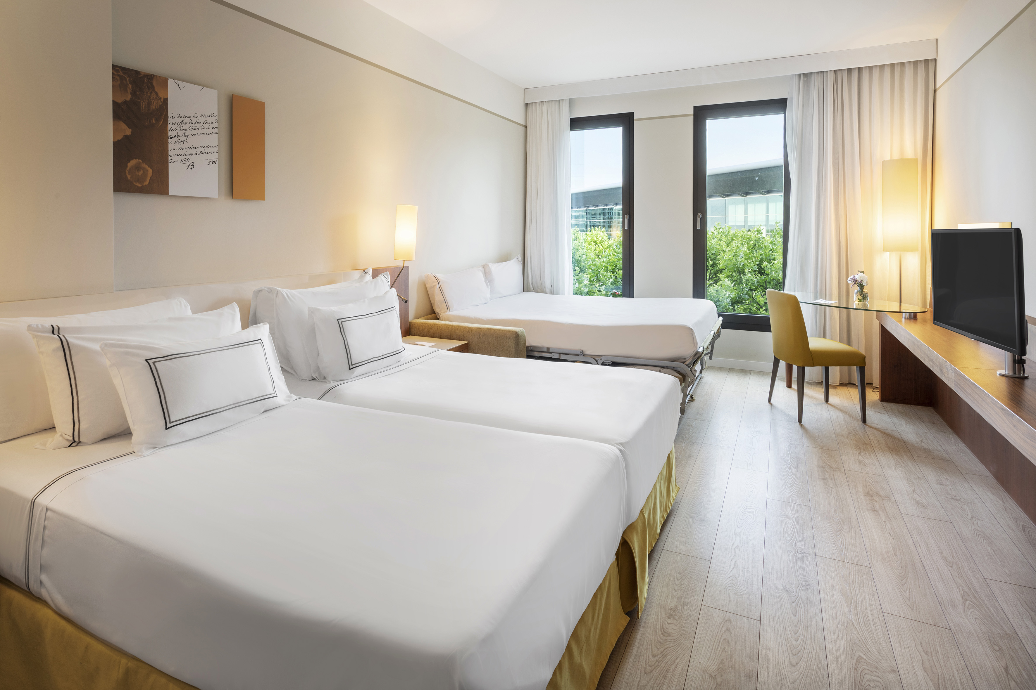 Spacious hotel room with twin beds, sofa bed, desk, and large bright windows.
