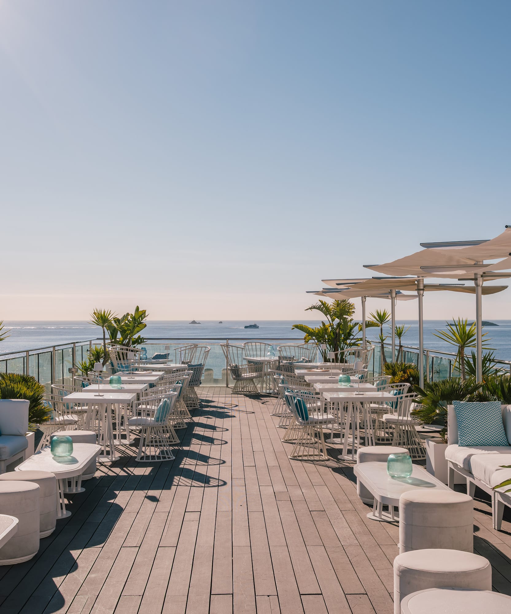 Rooftop lounge bar with white outdoor seating, sun umbrellas, and ocean views.
