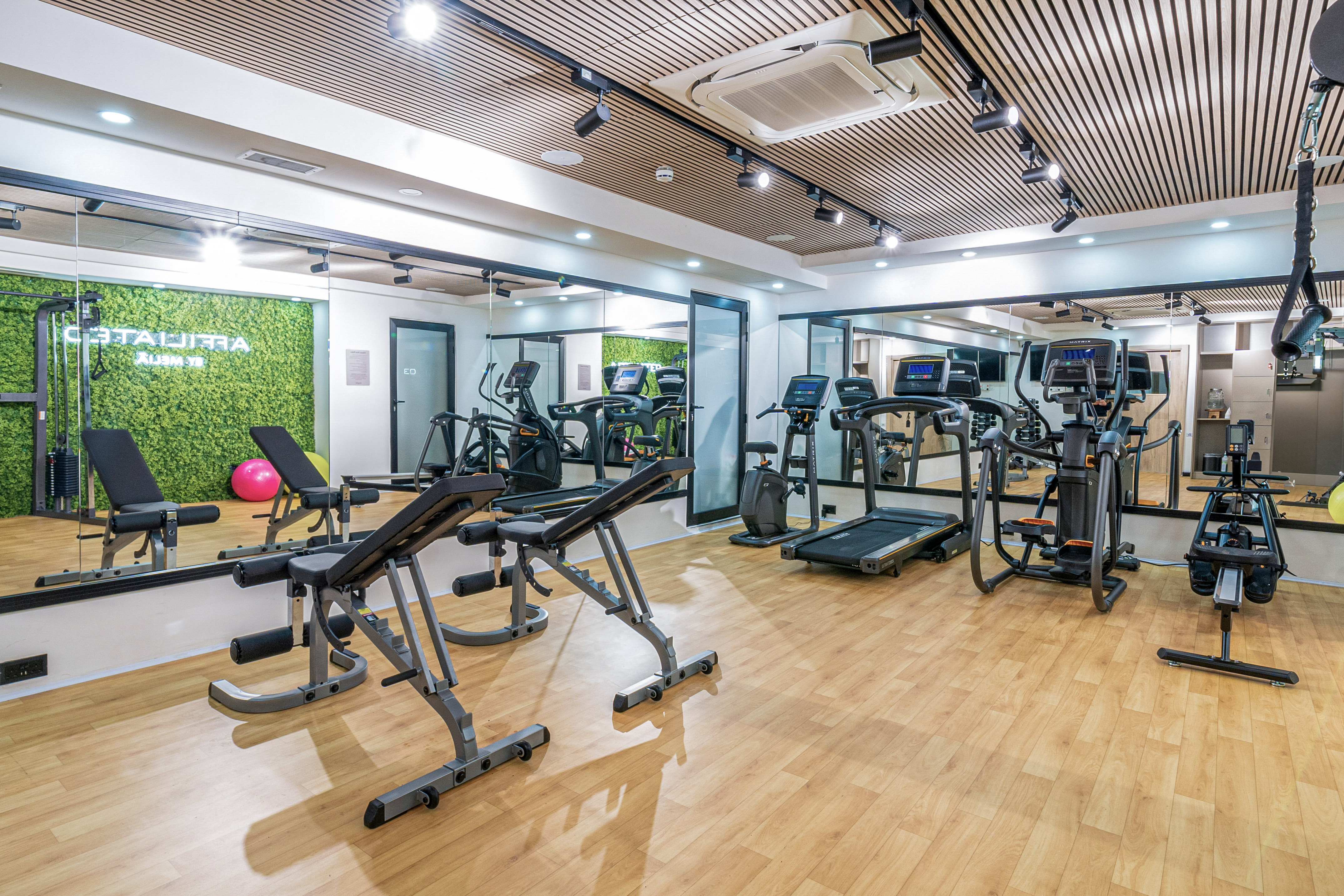 Modern gym with exercise equipment, mirrored walls, and green moss wall.