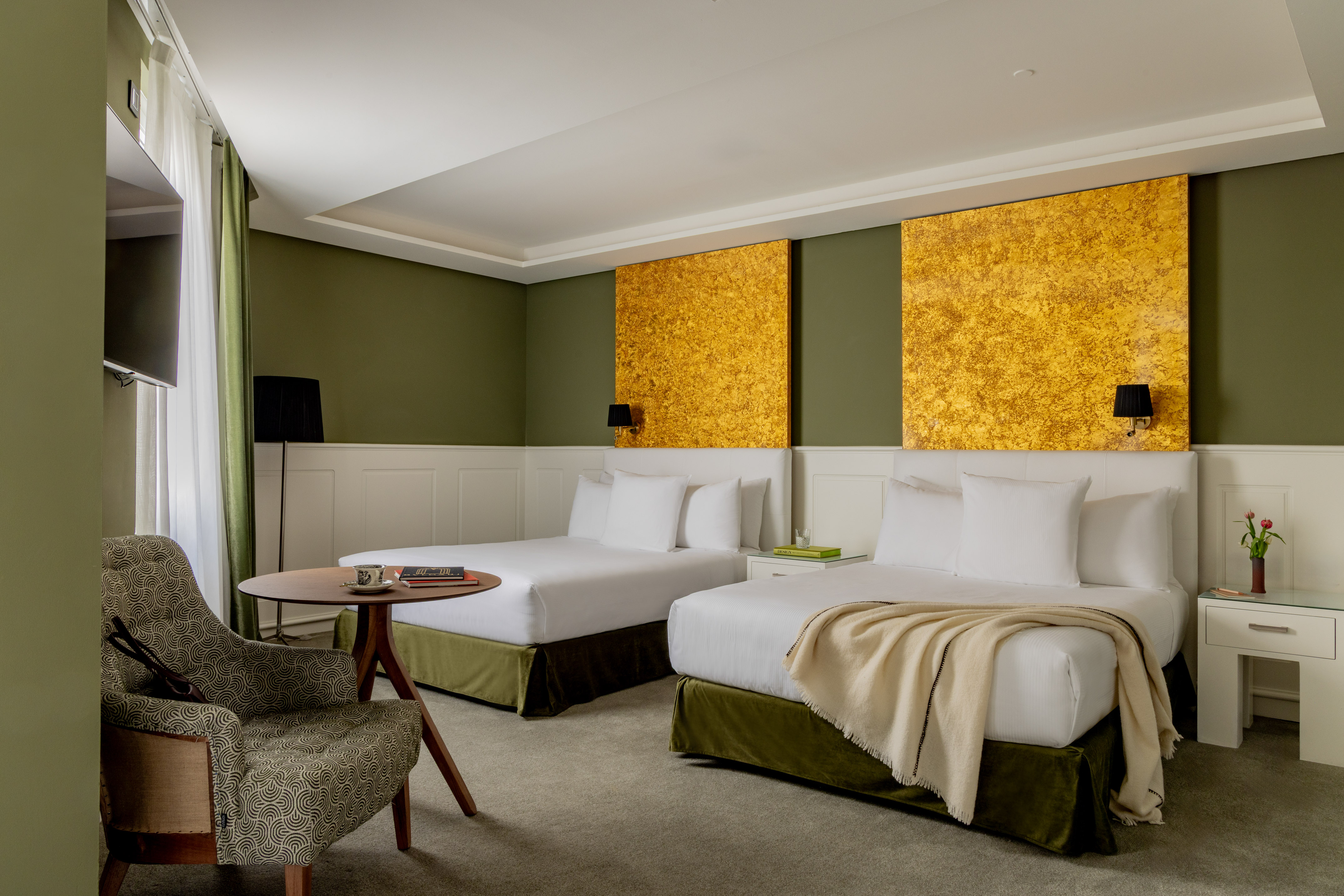 Modern hotel room with two queen beds, olive green walls, and golden art.