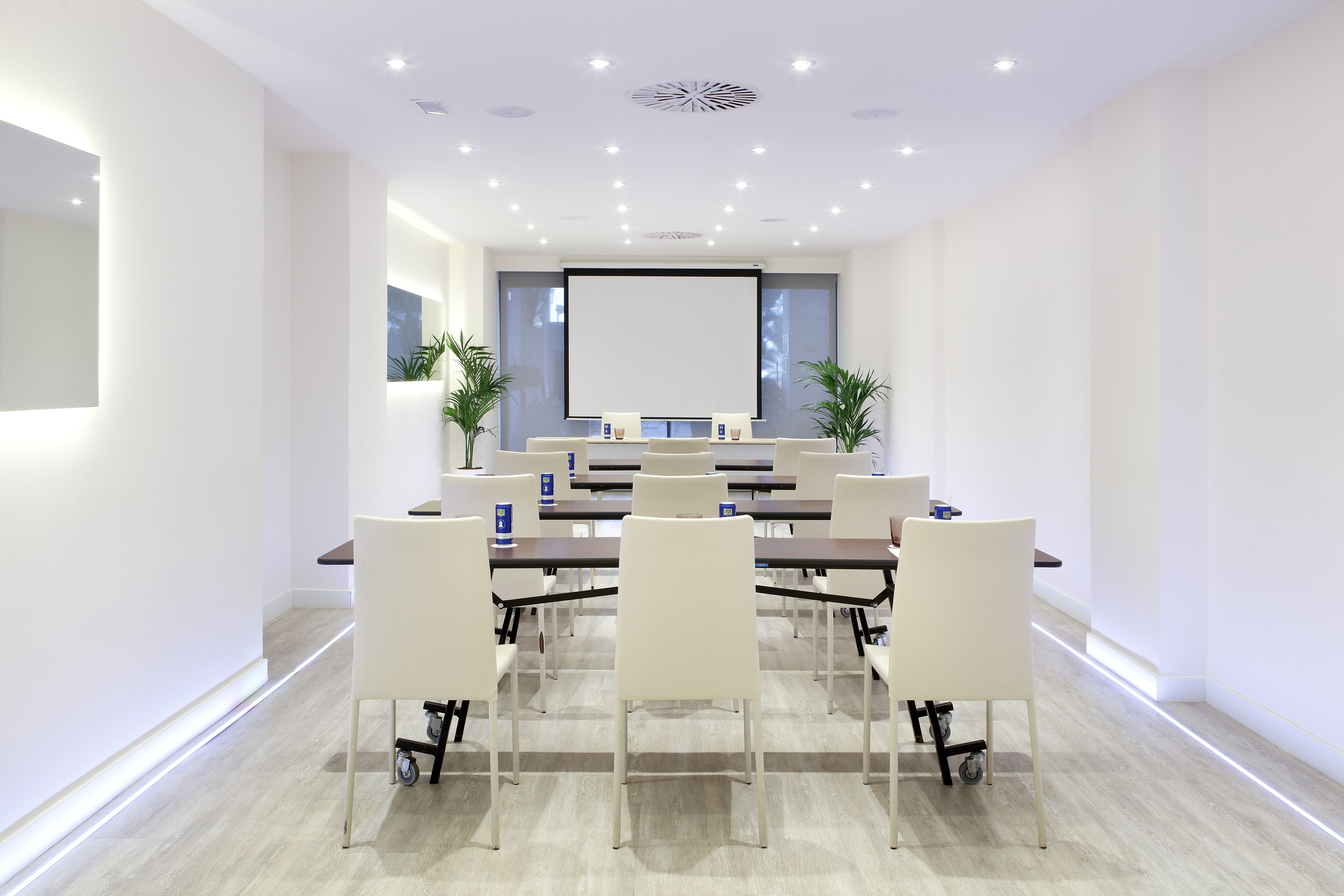 Modern, bright conference room with projector screen, tables, and white chairs.