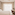 Modern hotel room with white bed, desk, coffee maker, and bright window.