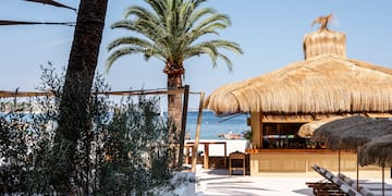 un bar sulla spiaggia con tetto di paglia e palme