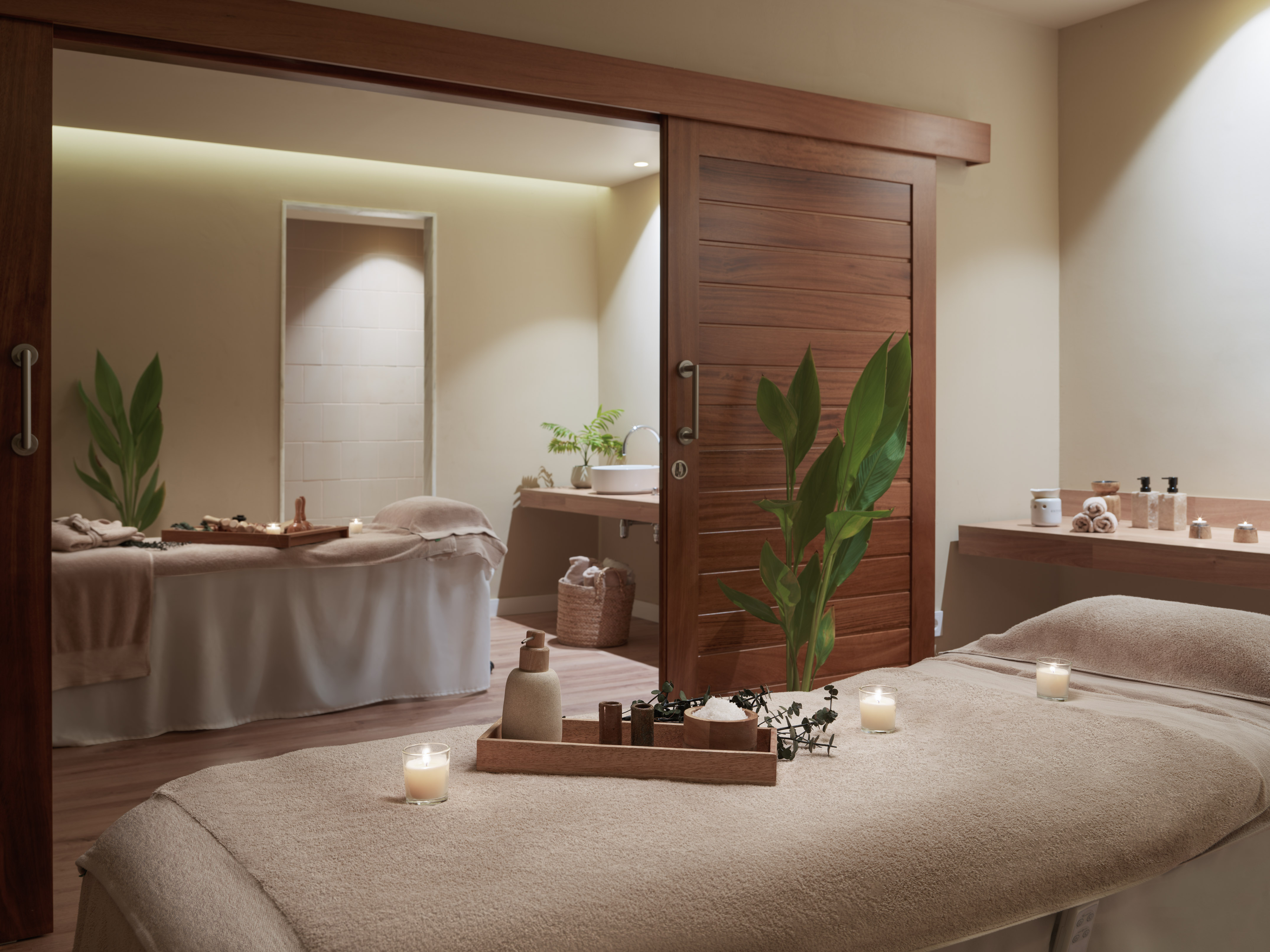Serene spa room with two massage beds, natural products, and lit candles.