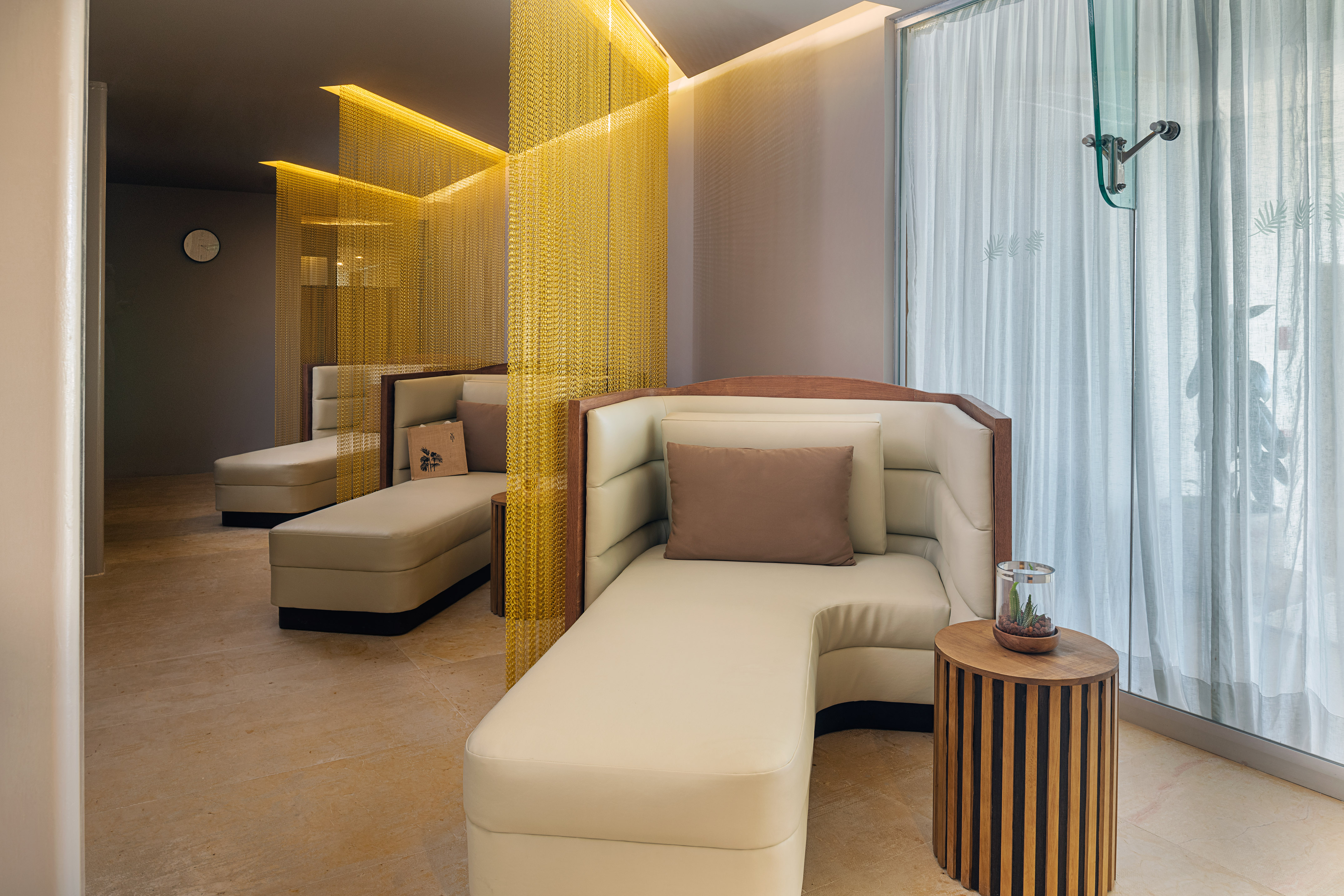 Luxury spa lounge with cream chaise lounges, gold chain dividers, soft lighting.