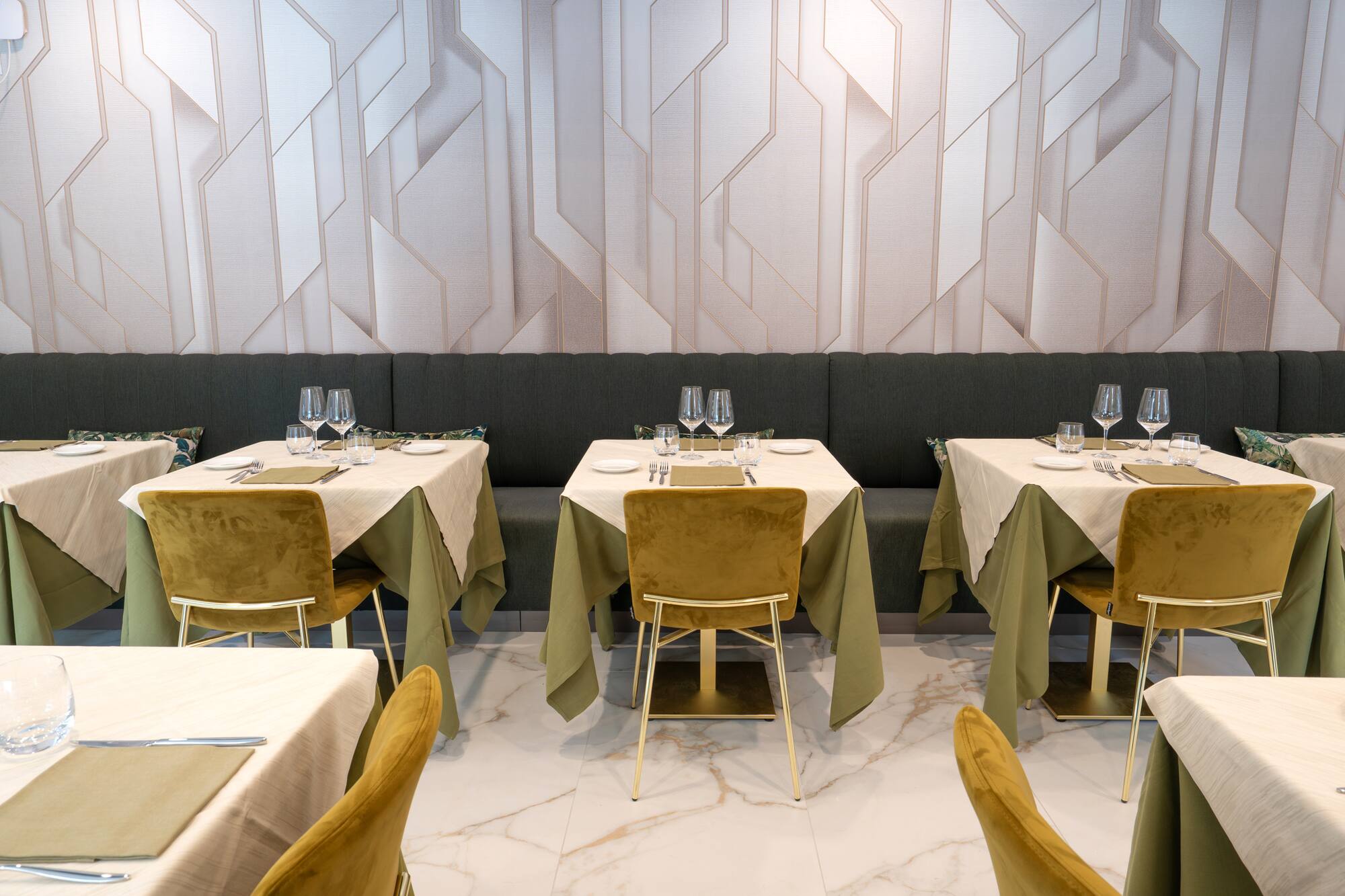 Modern restaurant dining room with elegant set tables, green velvet chairs, geometric wall.