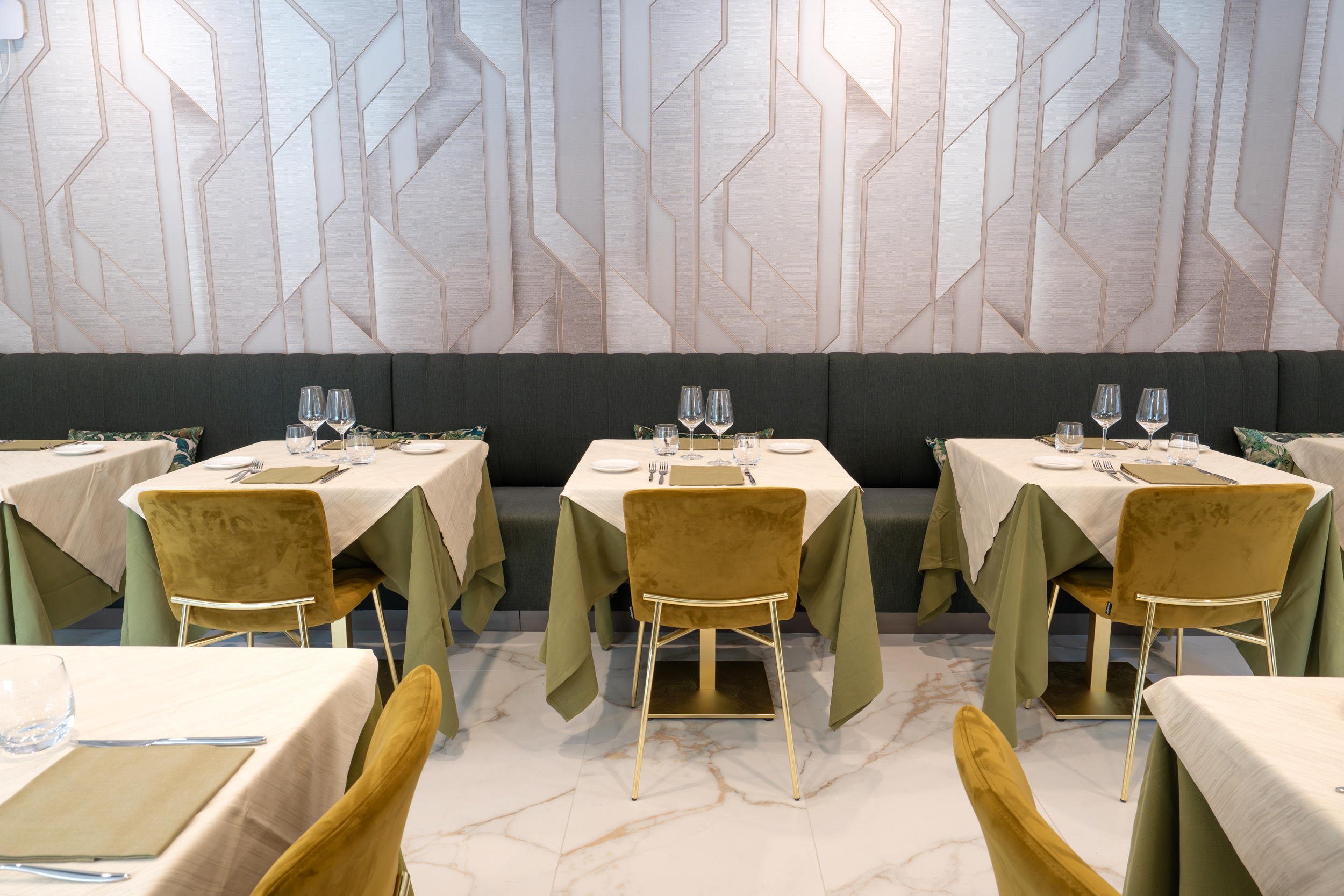 Modern restaurant dining room with elegant set tables, green velvet chairs, geometric wall.
