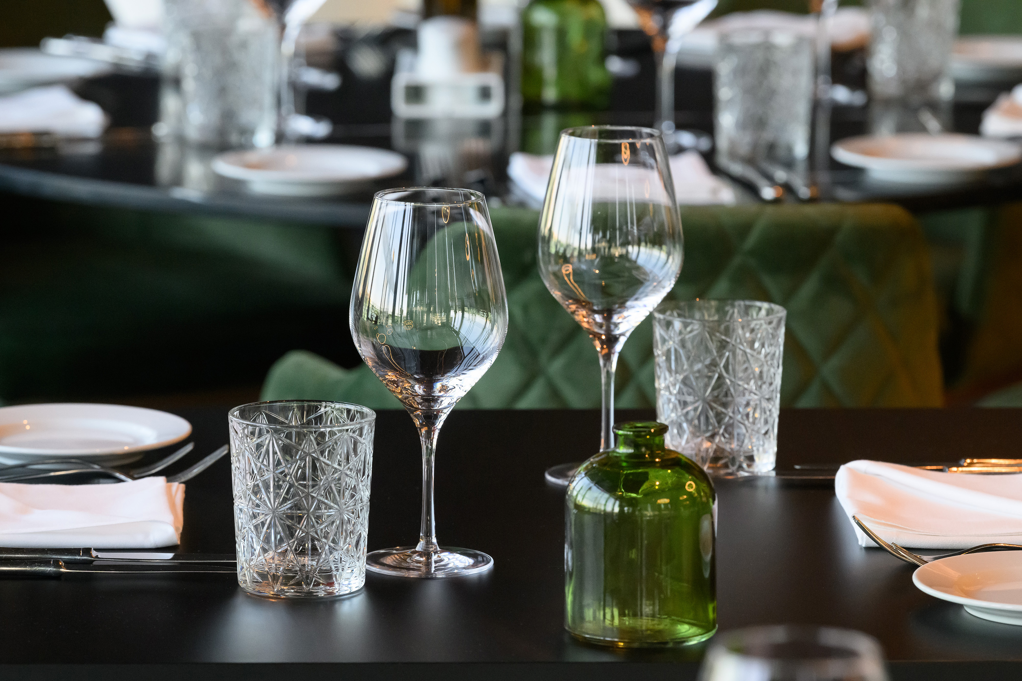 Set dining table with wine glasses, water glasses, plates, and green bottle.