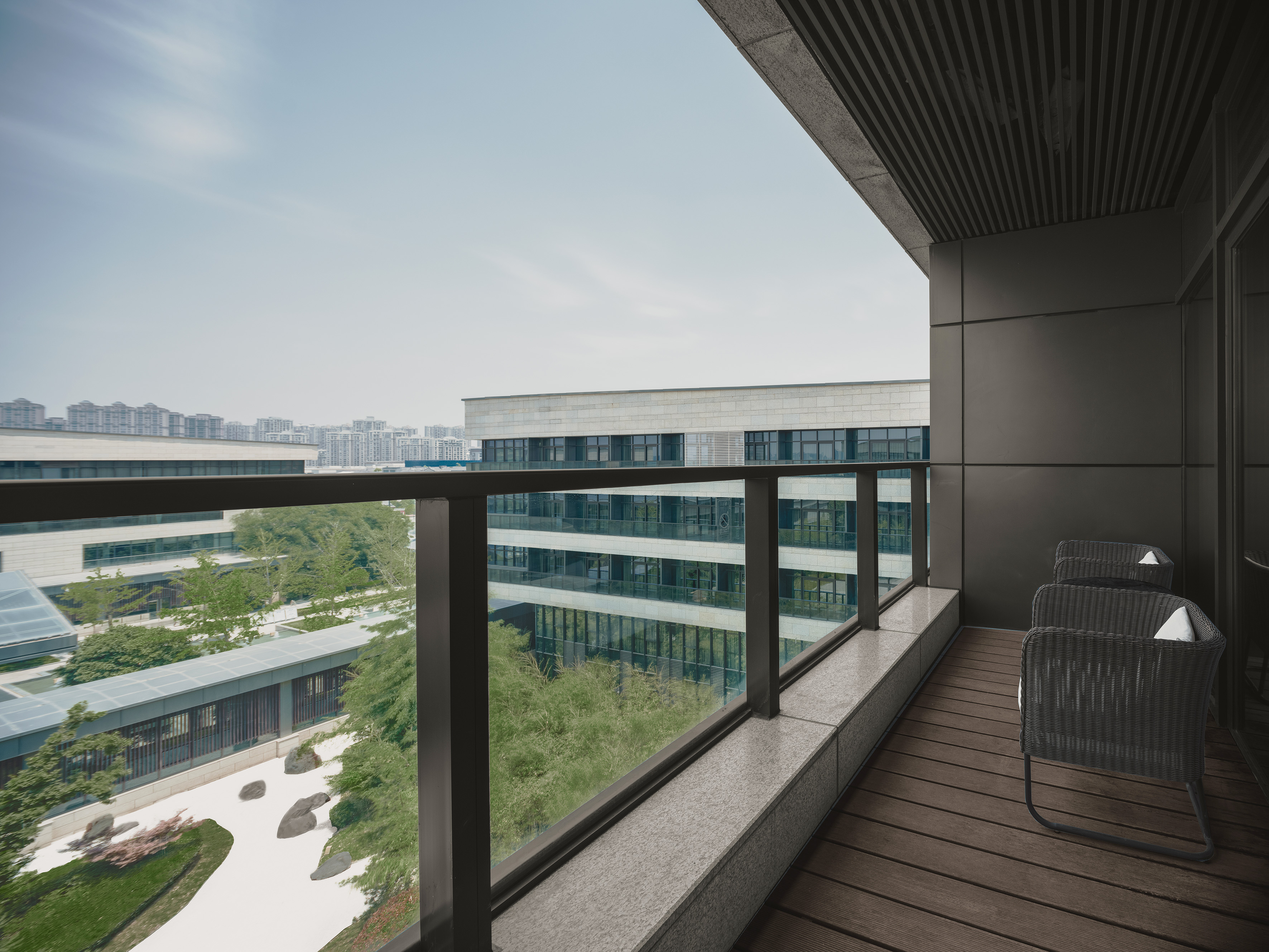 Modern balcony with chairs, city view, and landscaped garden.