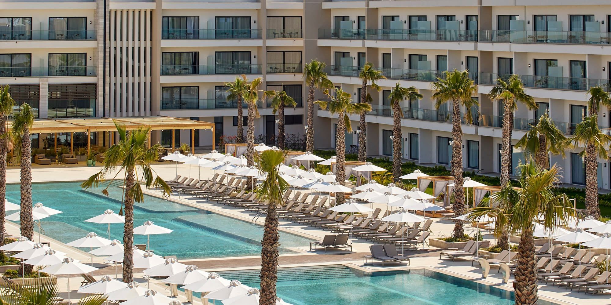 a pool with umbrellas and chairs in front of a hotel