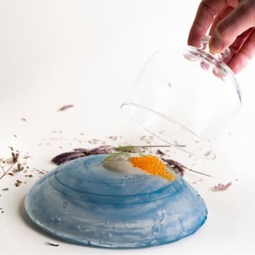 a hand holding a glass lid over a blue and white plate