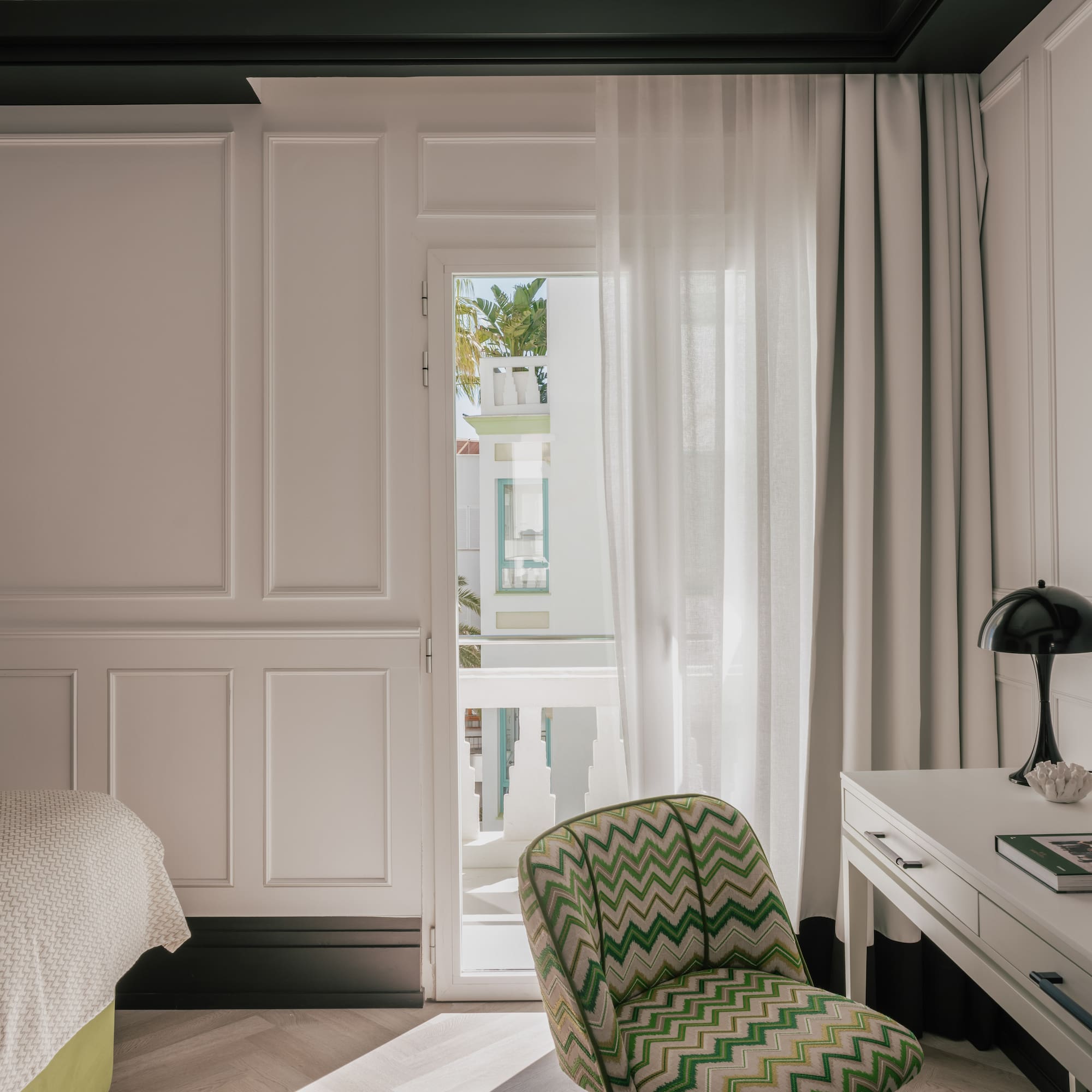 Modern hotel bedroom: white paneled walls, green chevron chair, balcony view.