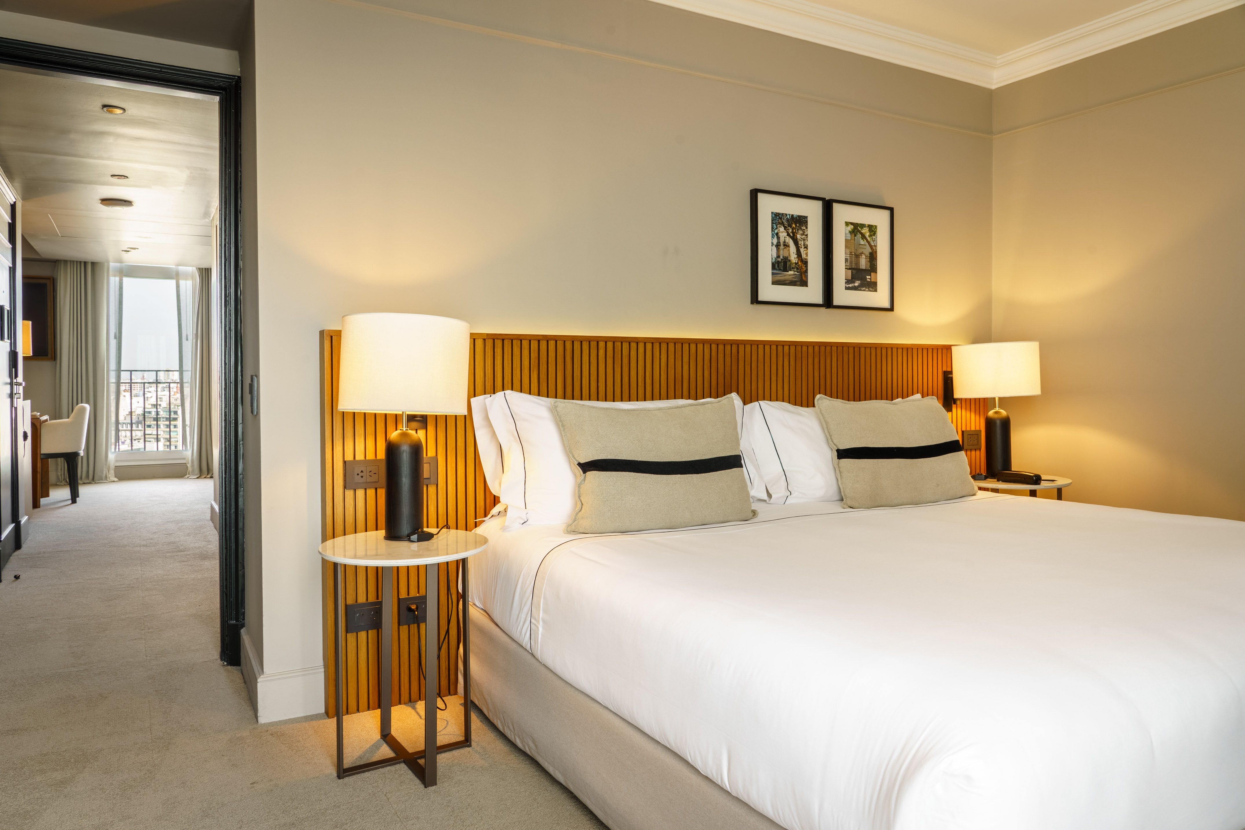 Modern hotel bedroom with king bed, wooden headboard, lamps, and balcony view.
