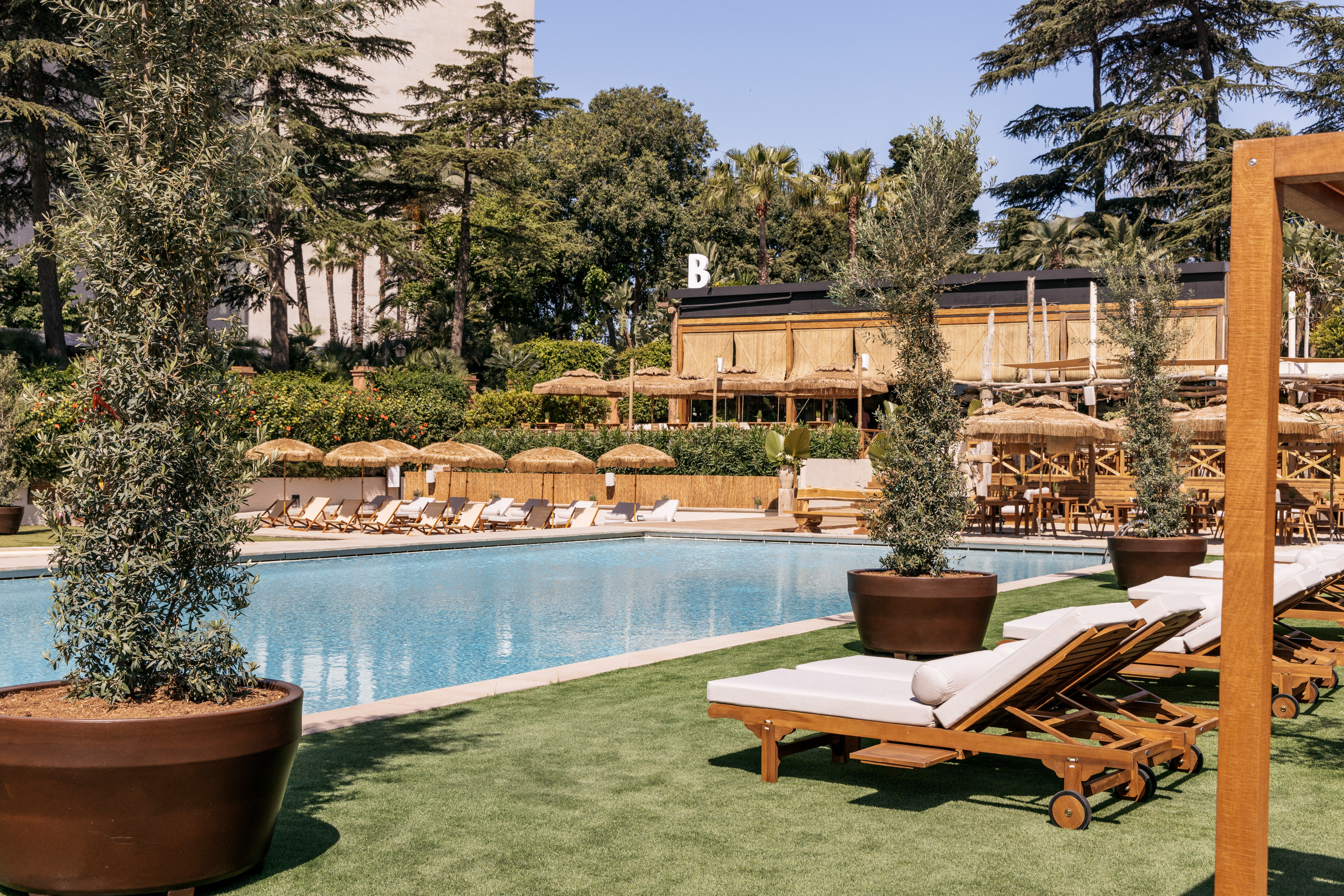 Resort swimming pool with sunbeds, straw umbrellas, and lush green landscaping.