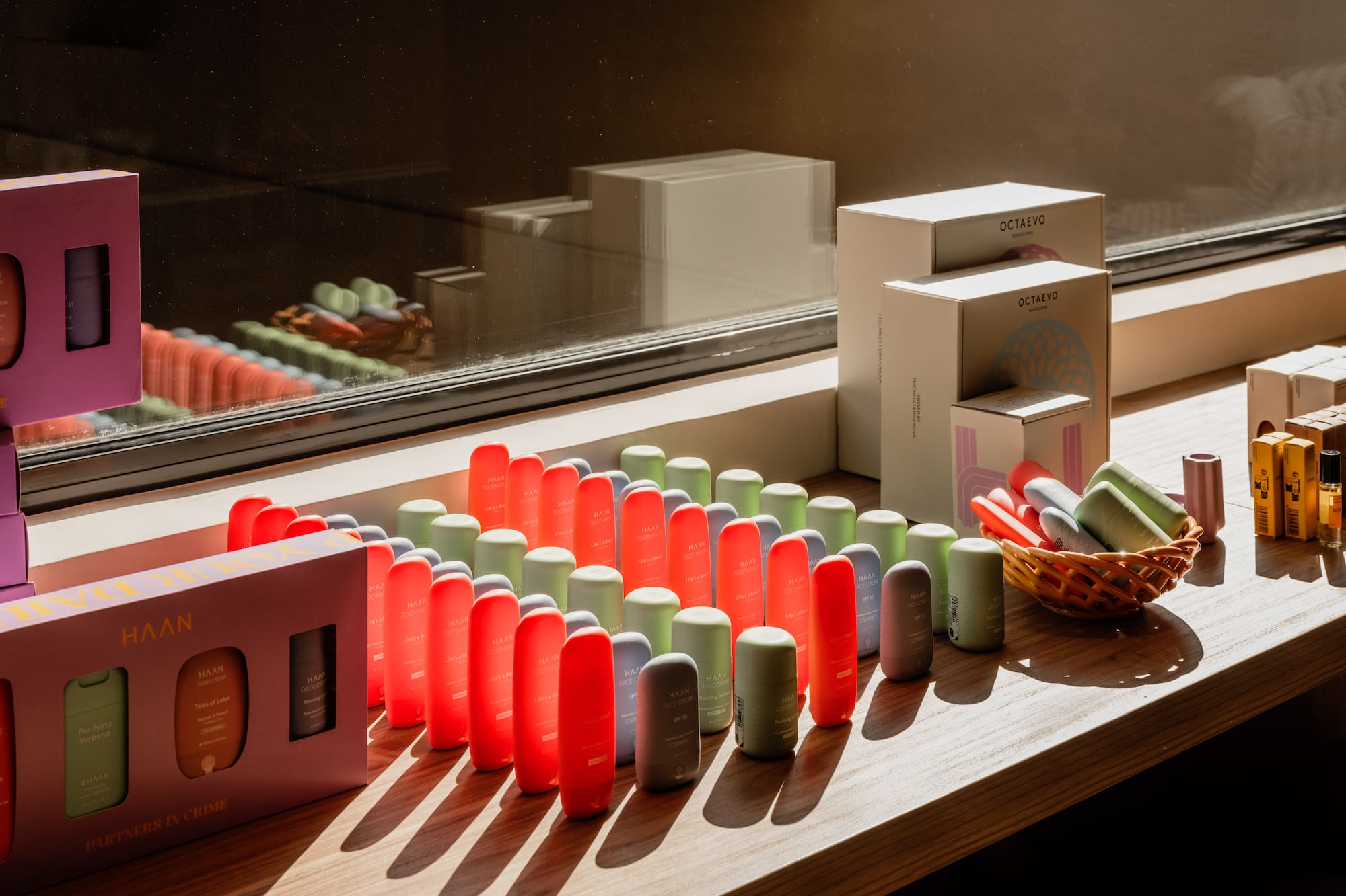 Colorful HAAN personal care products and Octaevo boxes on sunny wooden shelf.