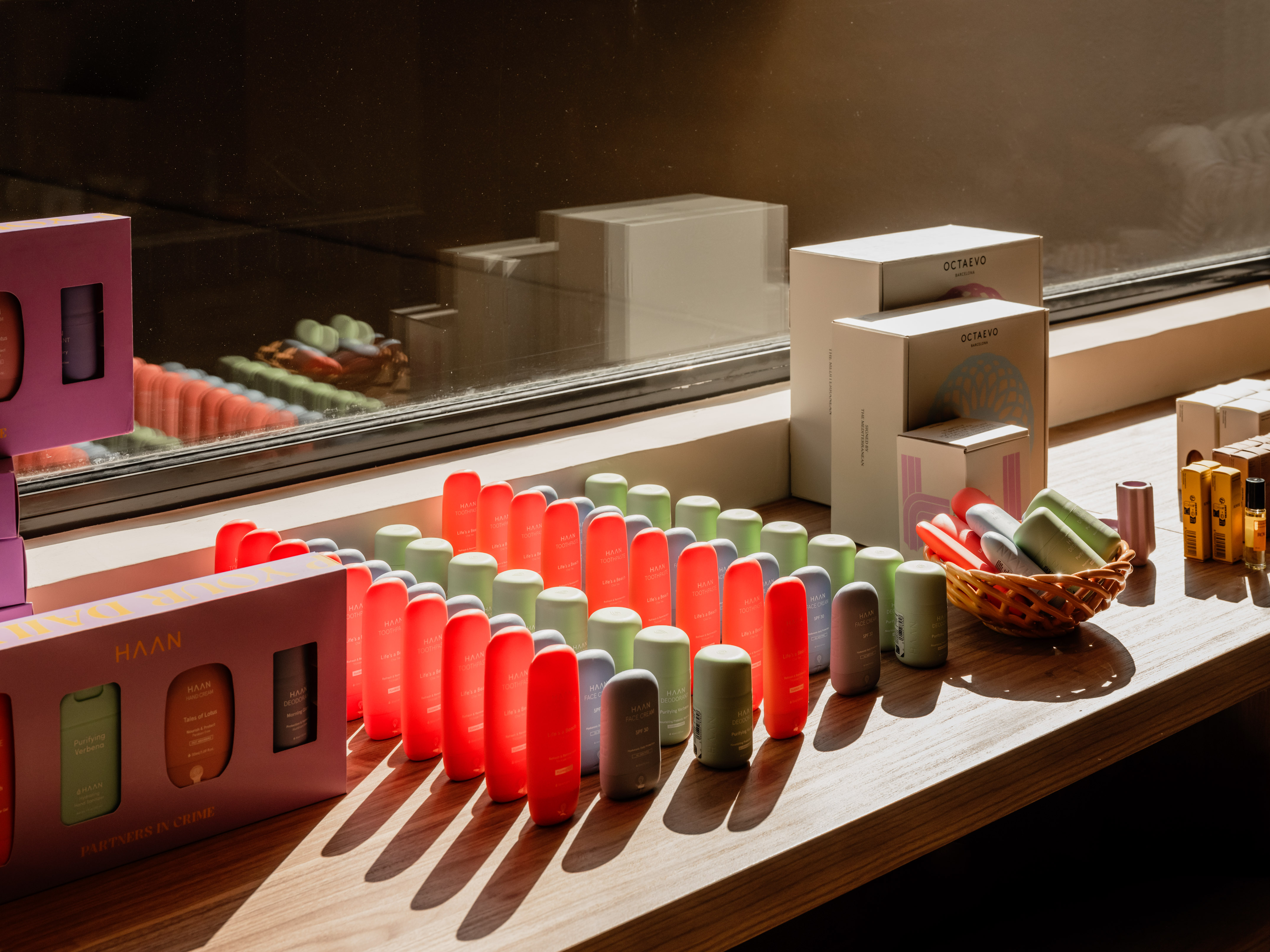 Colorful HAAN personal care products and Octaevo boxes on sunny wooden shelf.
