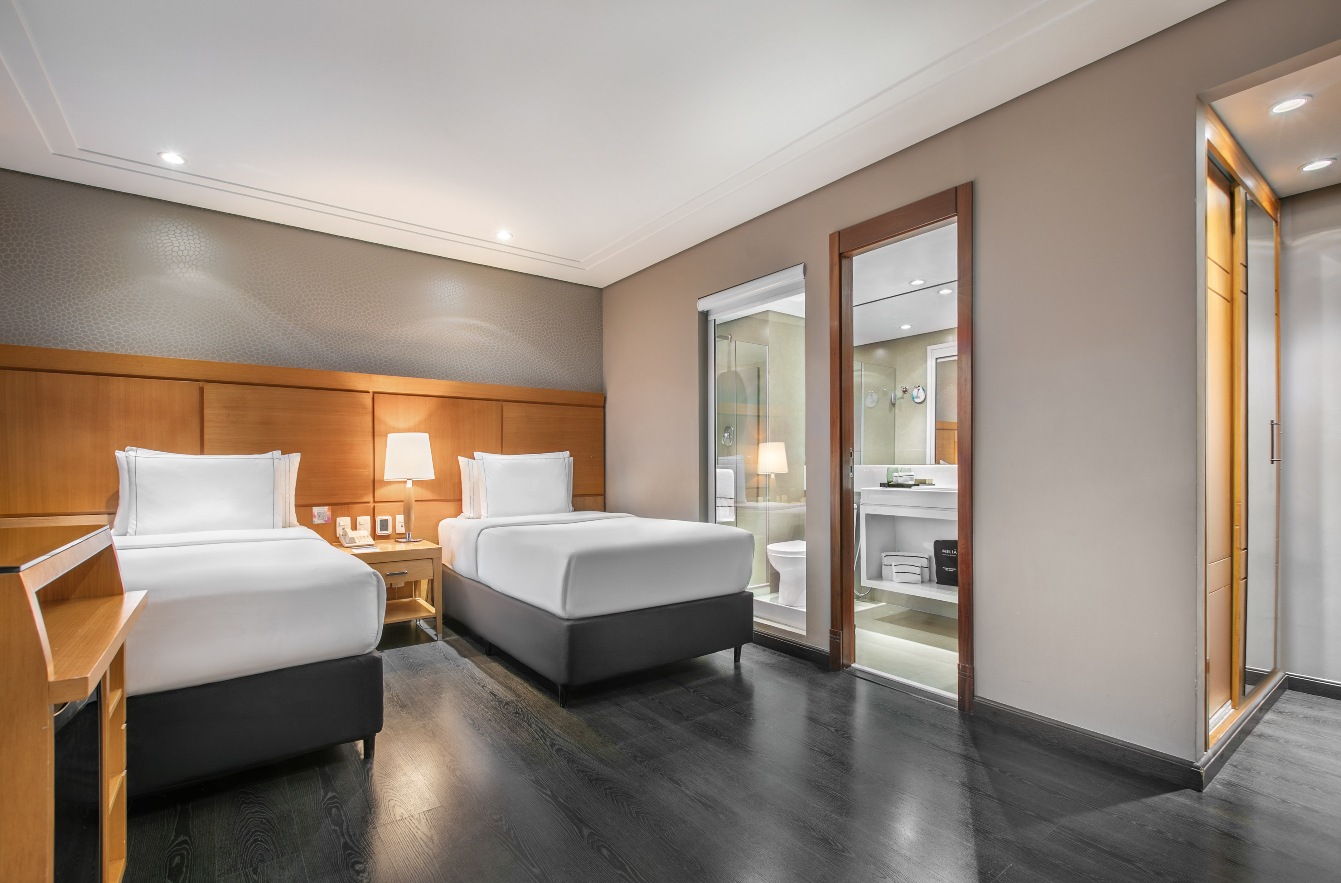 Modern hotel room with two twin beds, dark wood floor, and an en-suite bathroom.