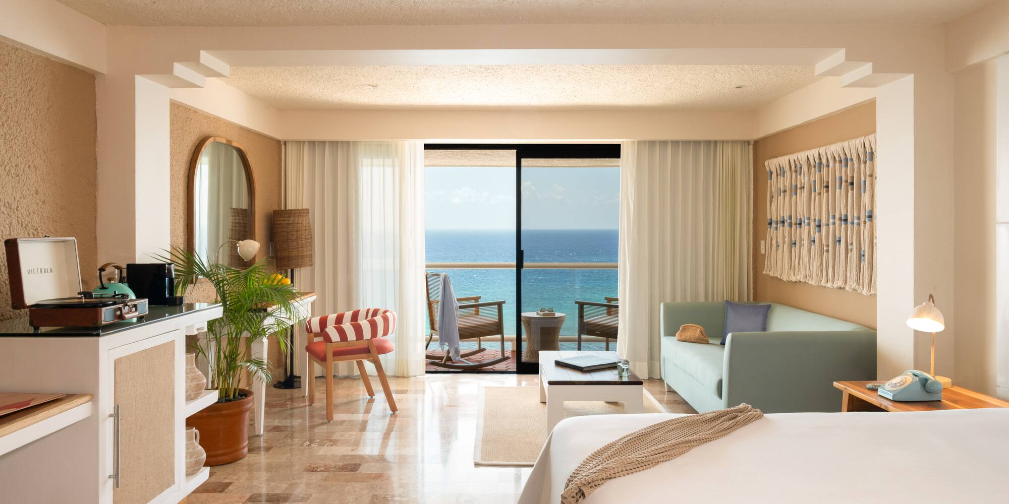 Hotel room with ocean view balcony, bed, and tropical-inspired decor.