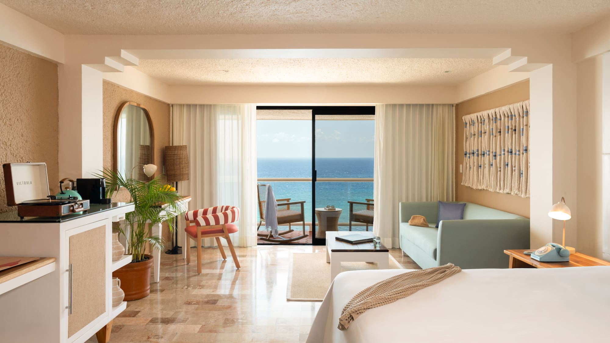 Hotel room with ocean view balcony, bed, and tropical-inspired decor.