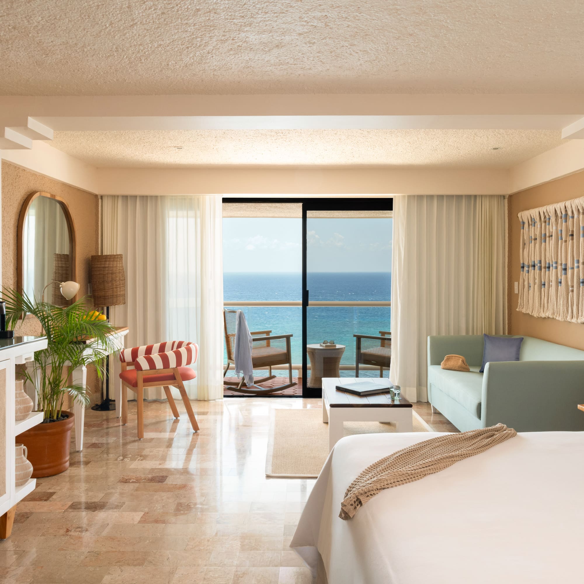 Hotel room with ocean view balcony, bed, and tropical-inspired decor.