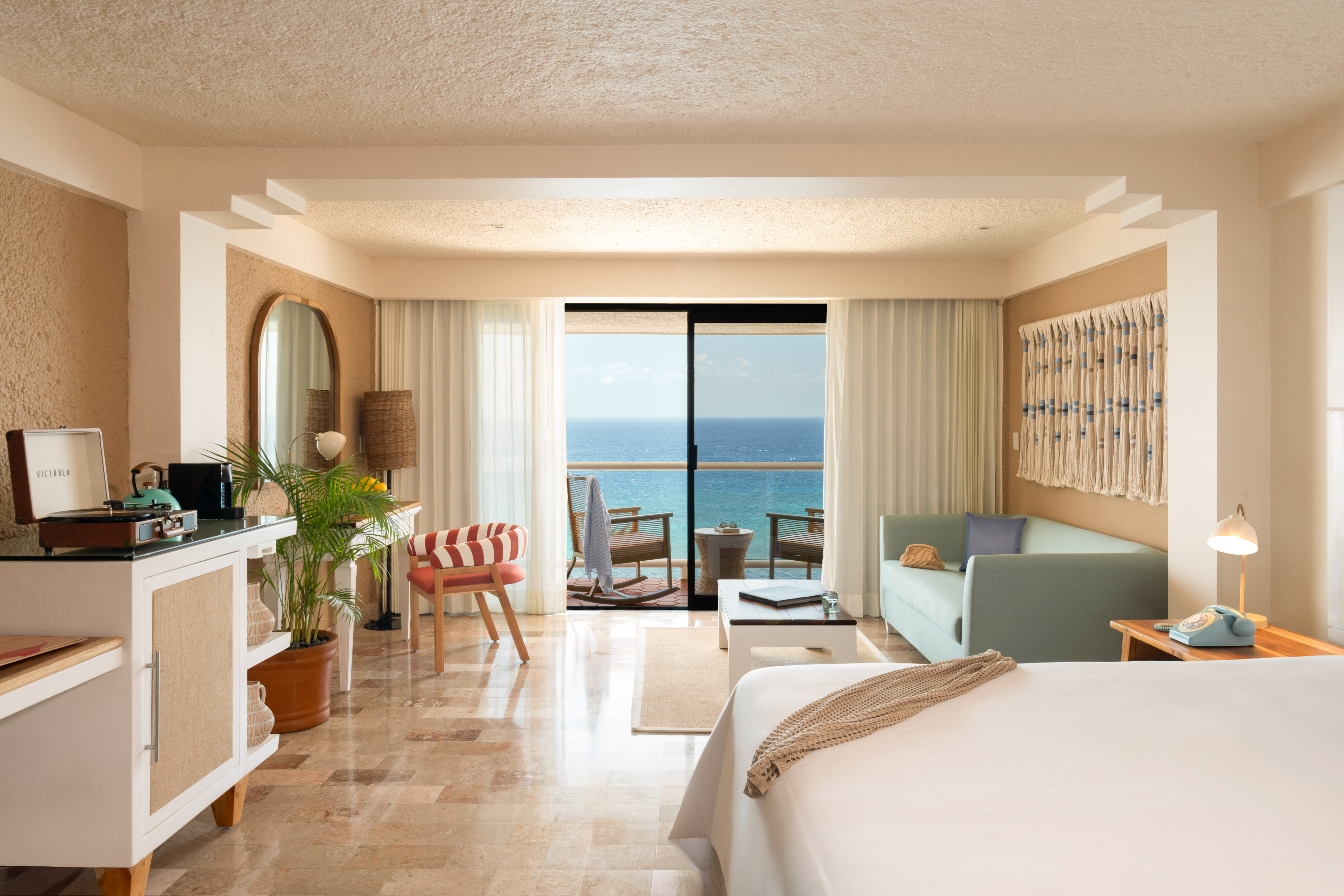 Hotel room with ocean view balcony, bed, and tropical-inspired decor.