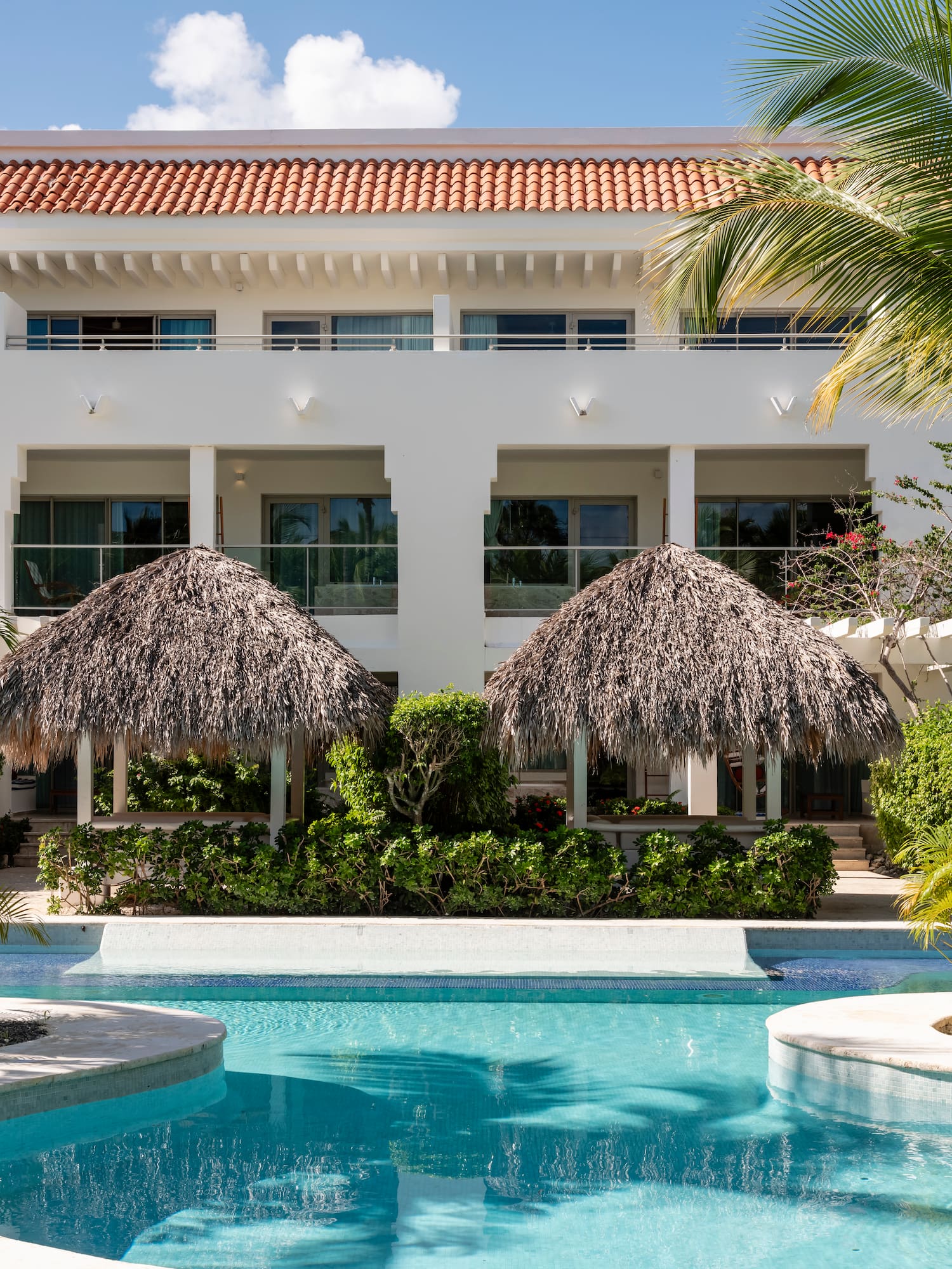 Tropical resort building with swimming pool, palm trees, and thatched gazebos. - Zel Punta Cana - All Suites, Punta Cana