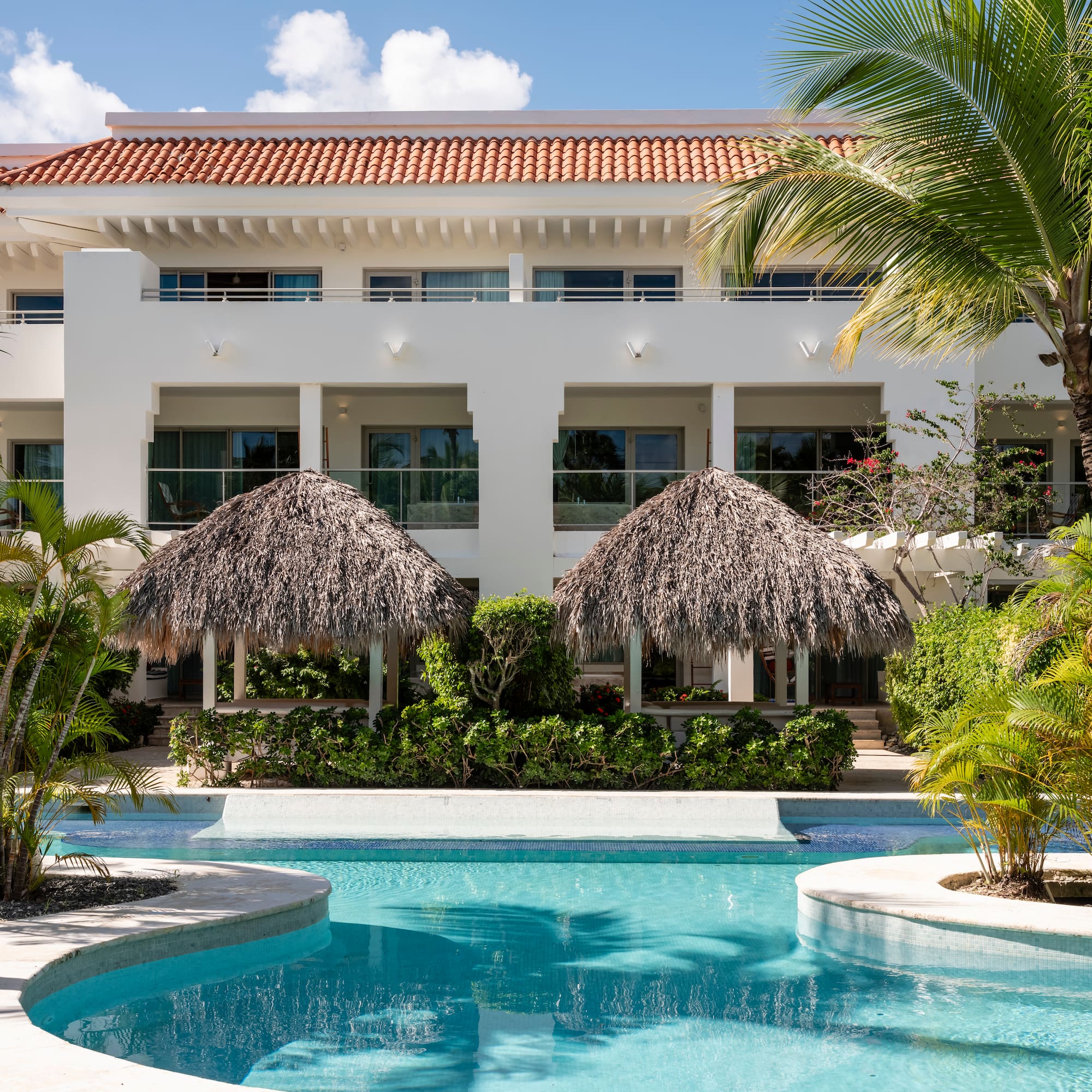 Tropical resort building with swimming pool, palm trees, and thatched gazebos. - Zel Punta Cana - All Suites, Punta Cana
