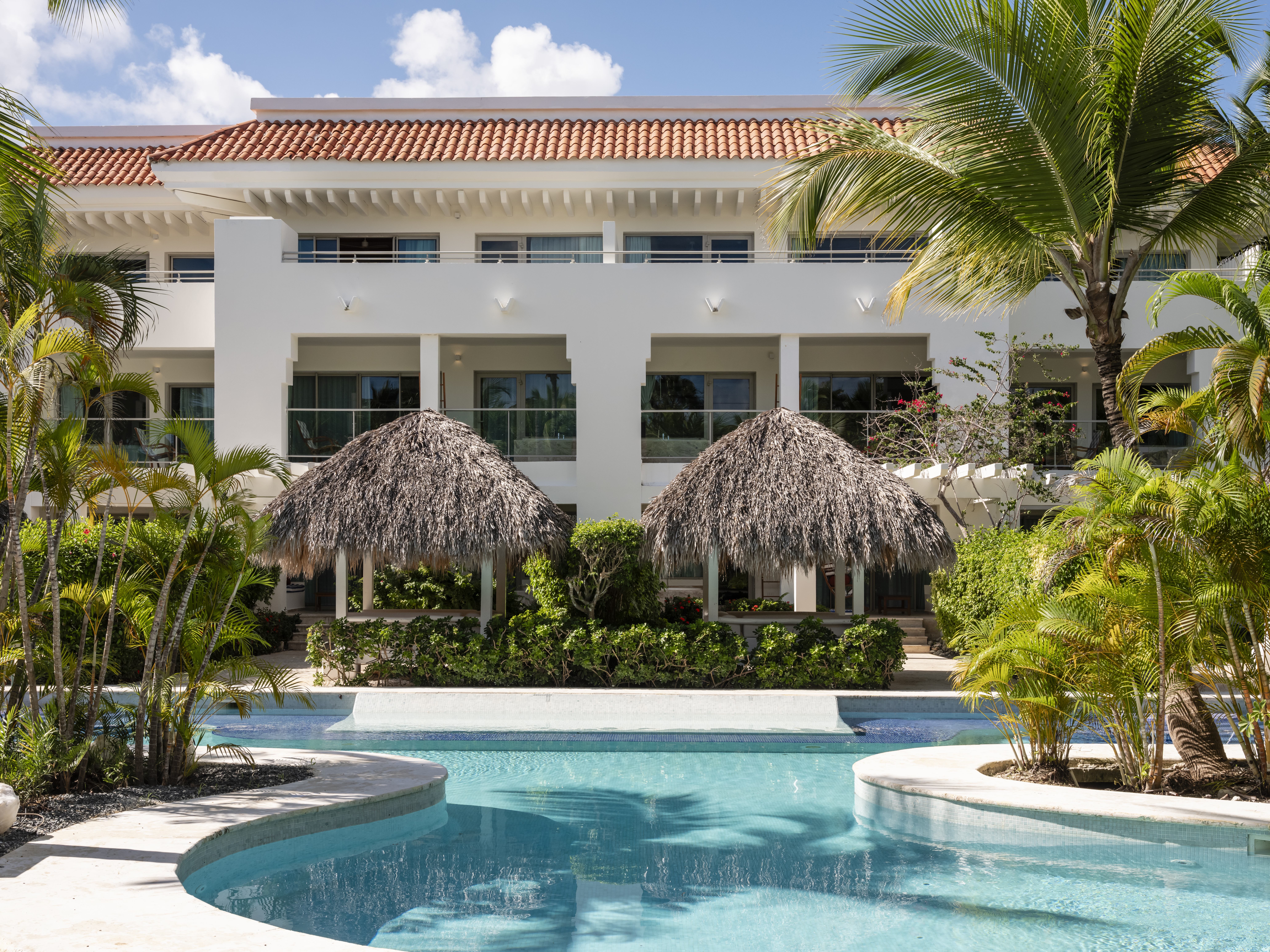 Tropical resort building with swimming pool, palm trees, and thatched gazebos. - Zel Punta Cana - All Suites, ปุนตา กานา