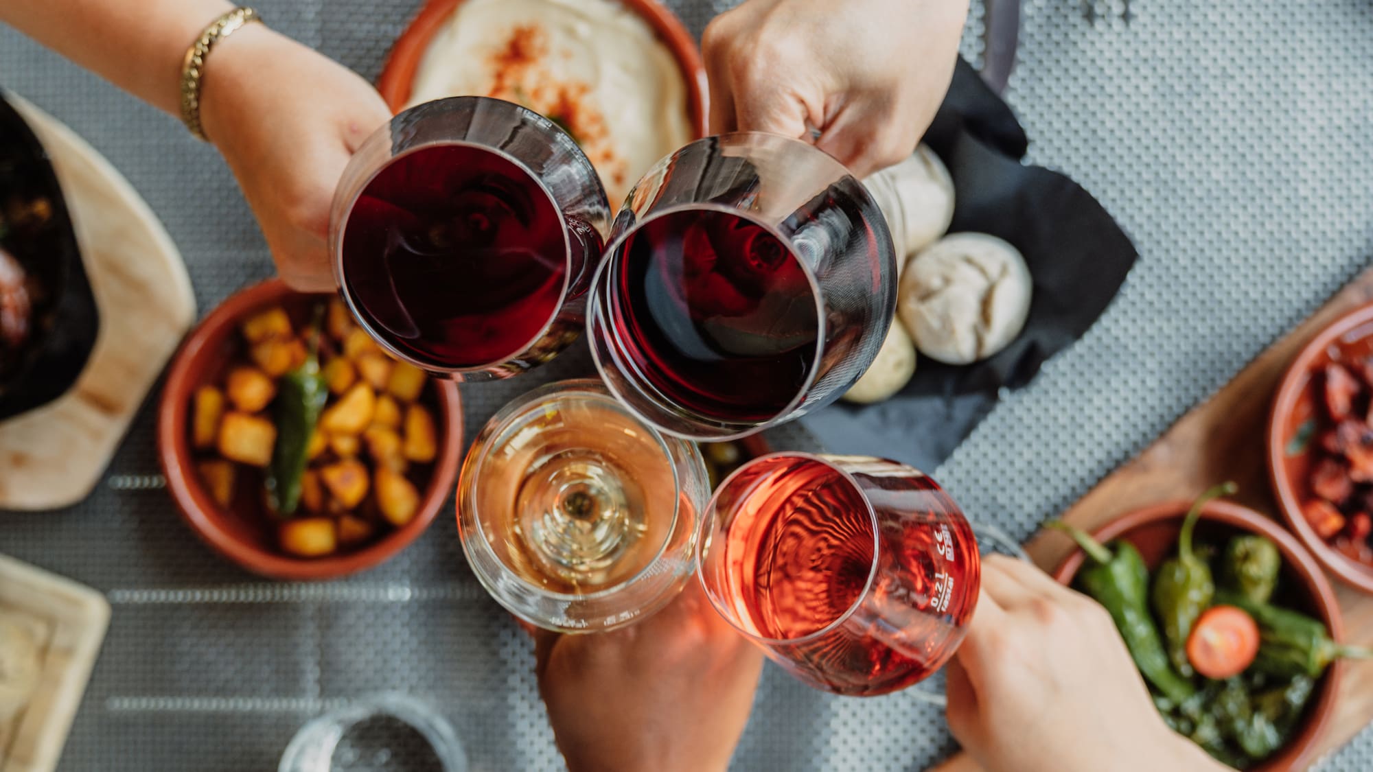 Hands toasting with red, rose, and white wine glasses over tapas dishes.