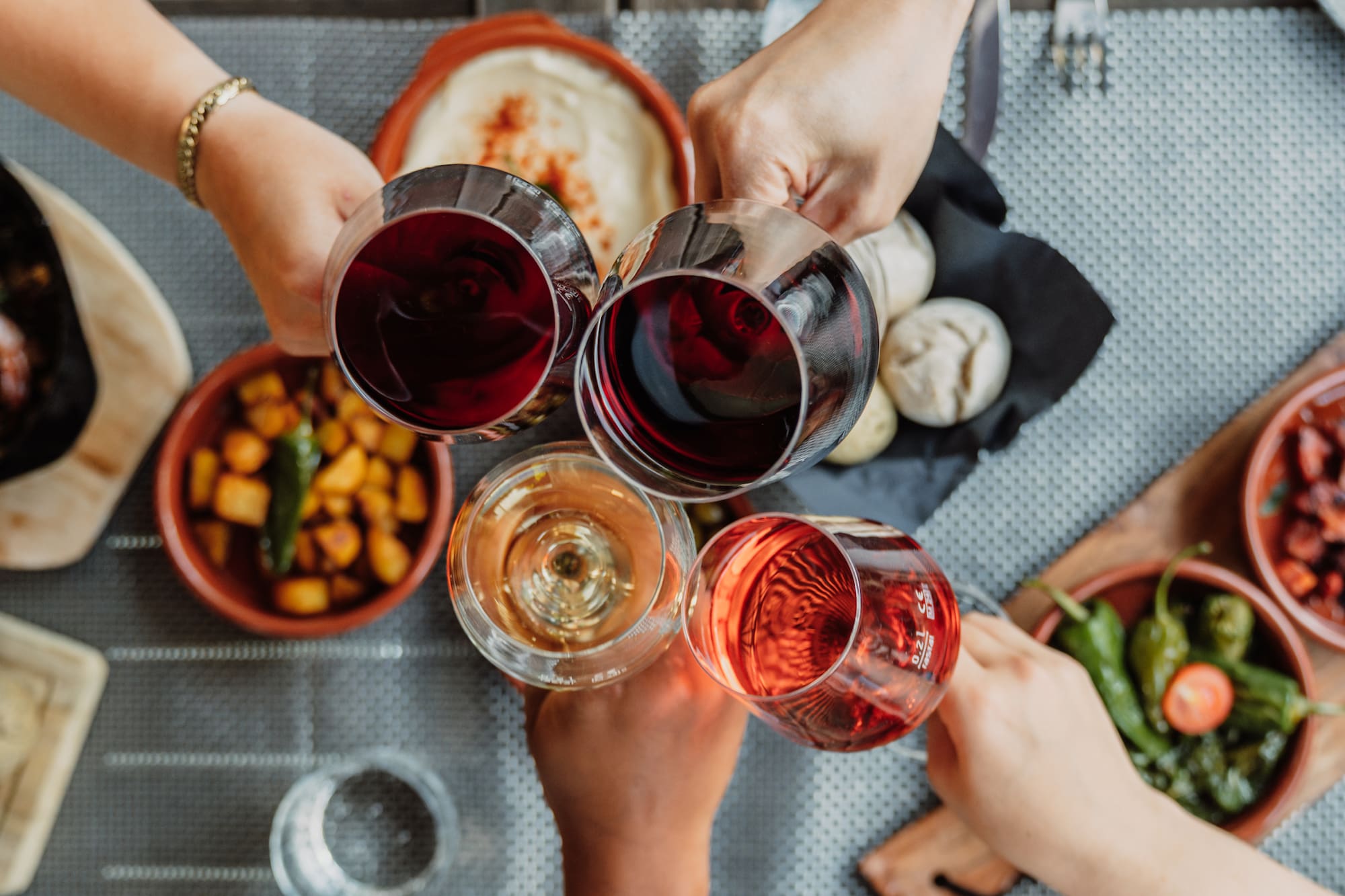 Hands toasting with red, rose, and white wine glasses over tapas dishes.