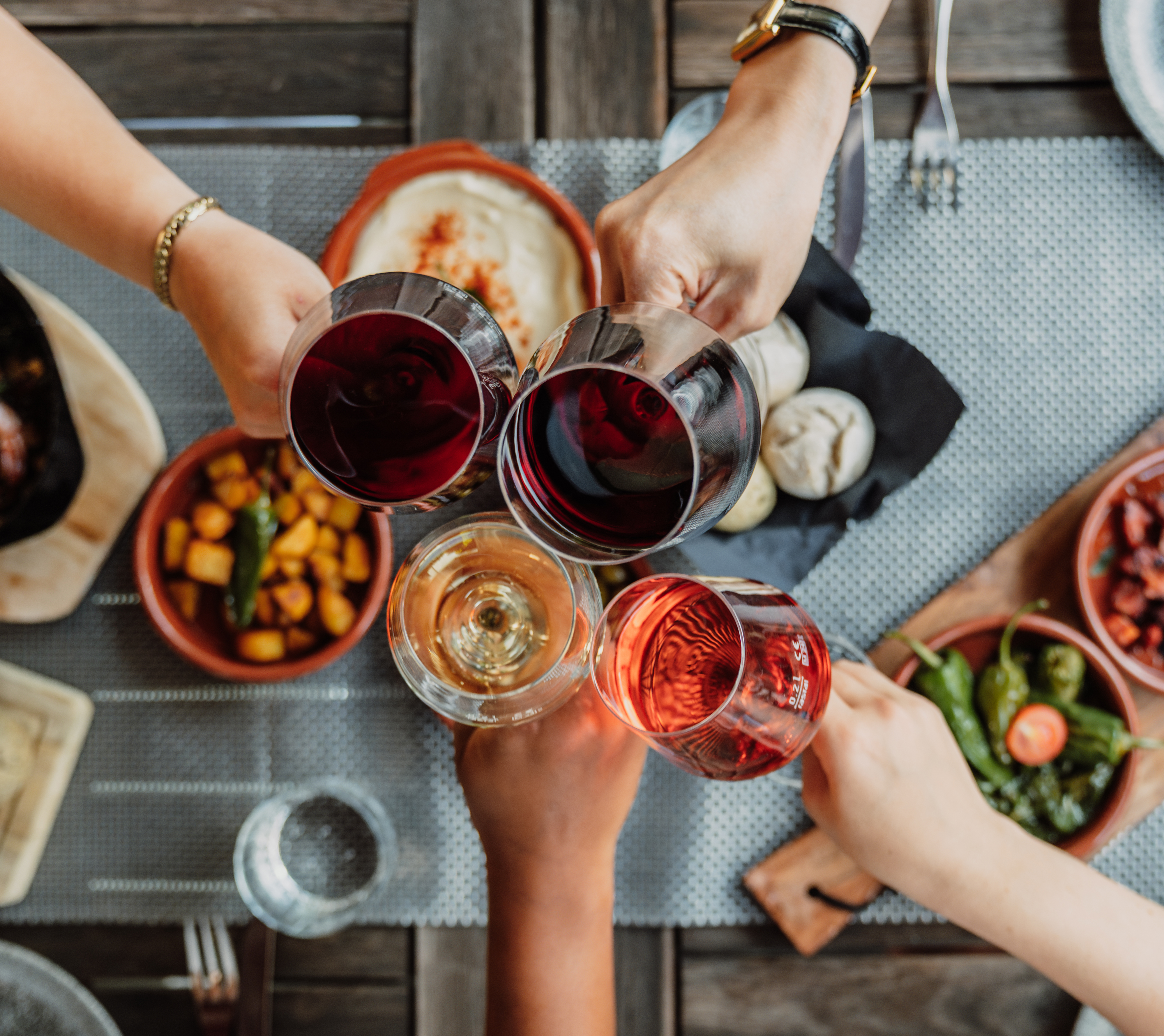 Hands toasting with red, rose, and white wine glasses over tapas dishes.