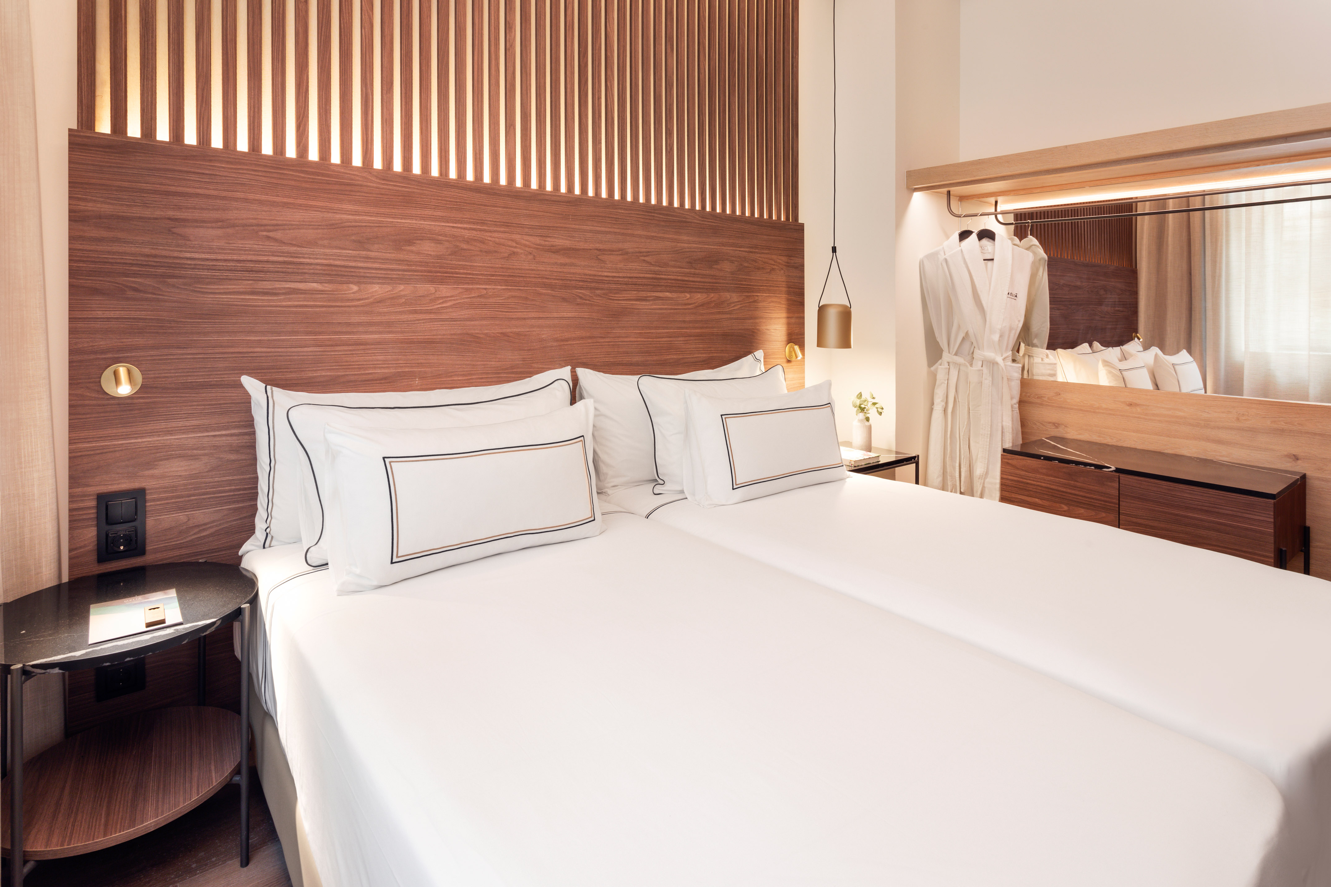Elegant hotel room with twin beds, dark wood headboard, and a white bathrobe.