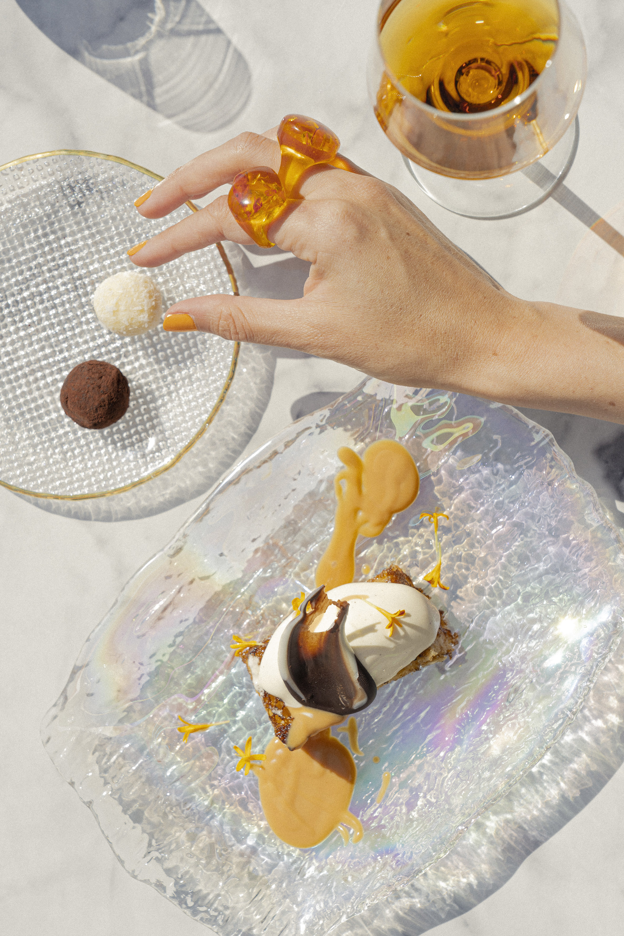 Elegant dessert, chocolate truffles, amber drink, hand with amber rings.
