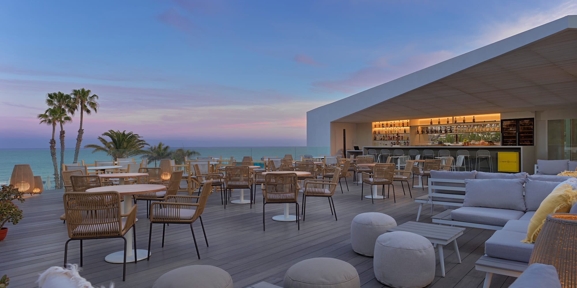a patio with tables and chairs on a deck with a bar and palm trees