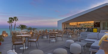 a patio with tables and chairs on a deck with a bar and palm trees
