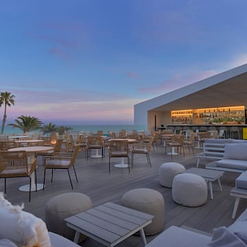 a patio with tables and chairs on a deck with a bar and palm trees