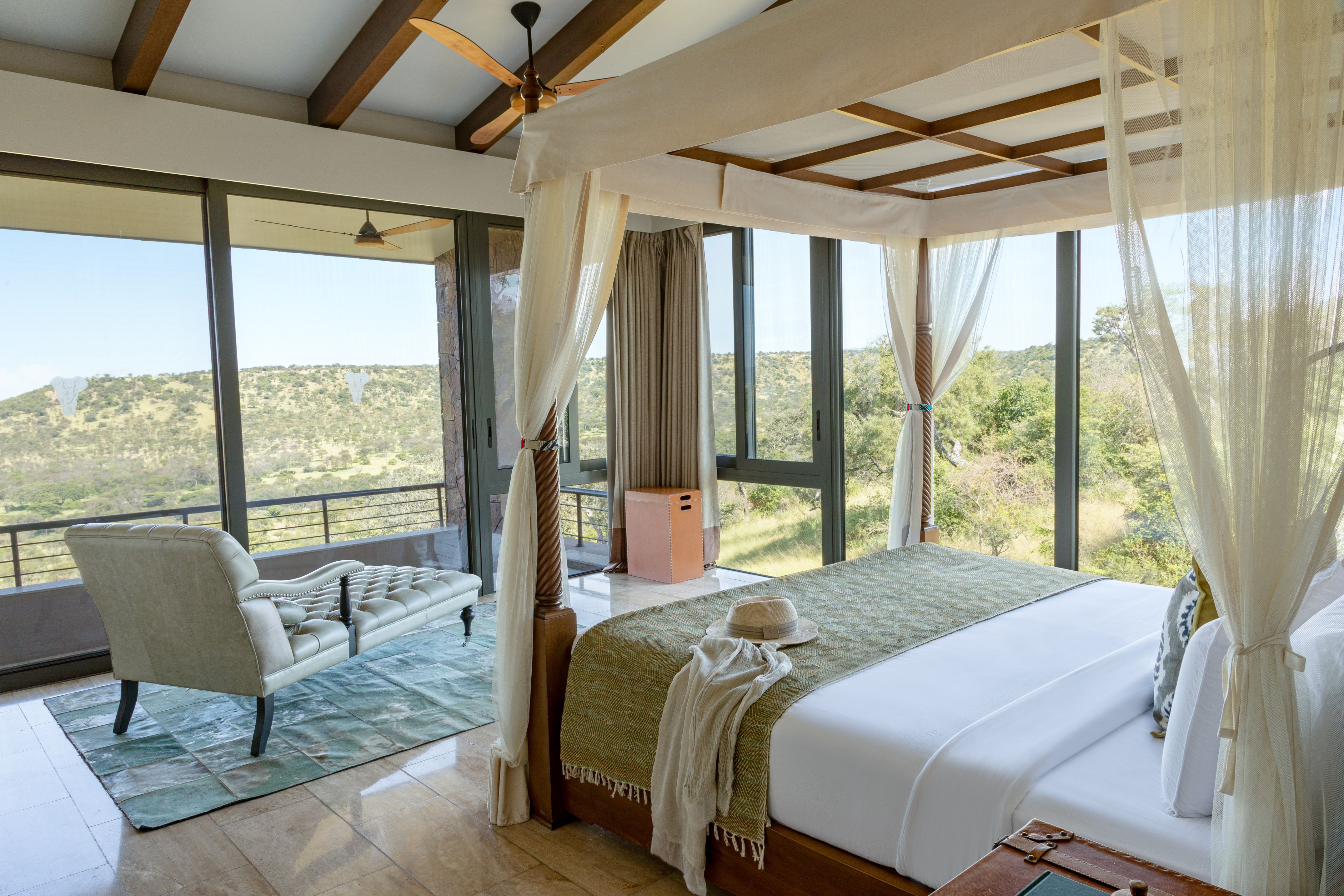 Luxury safari lodge bedroom with canopy bed and panoramic mountain views.