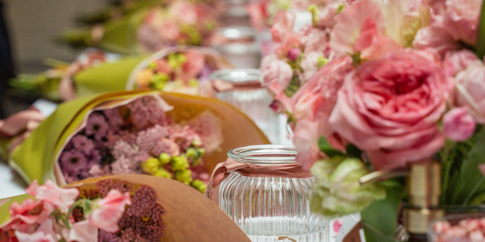 Pink floral bouquets, wrapped flowers, and lit candles on an event table.