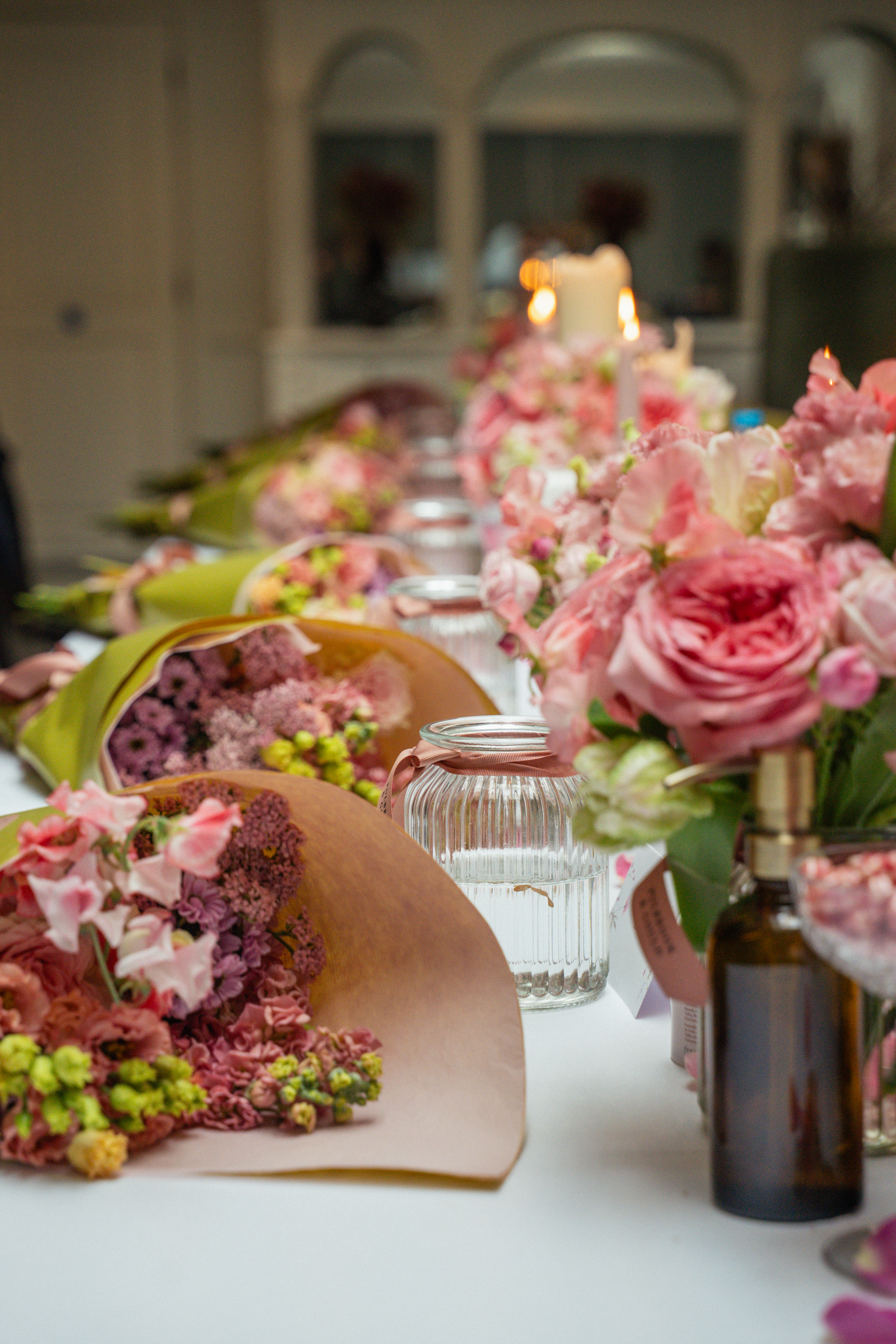 Pink floral bouquets, wrapped flowers, and lit candles on an event table.