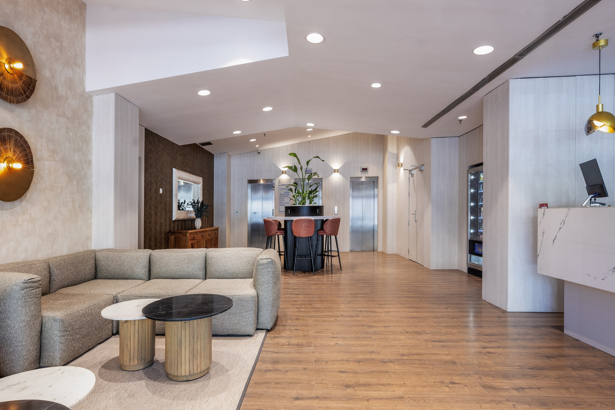 Modern hotel lobby with sofa lounge, marble reception desk, and elevators.