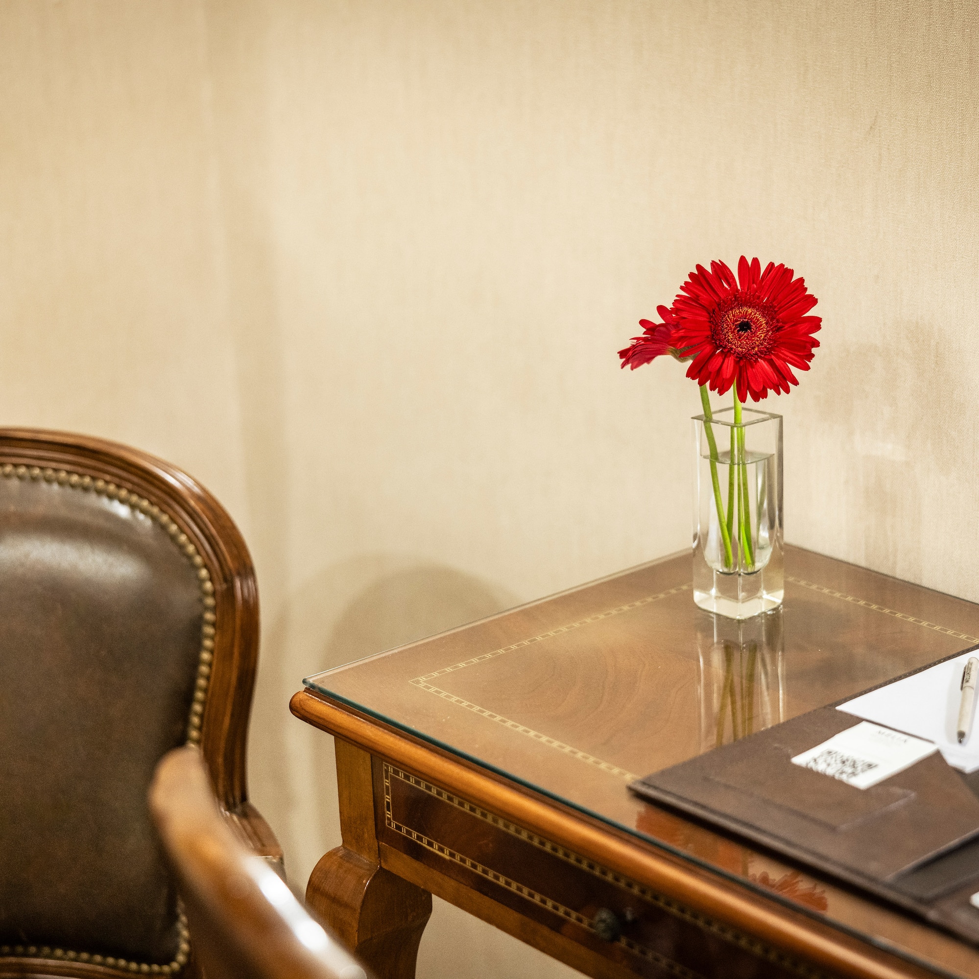 a red flower in a glass vase on a desk