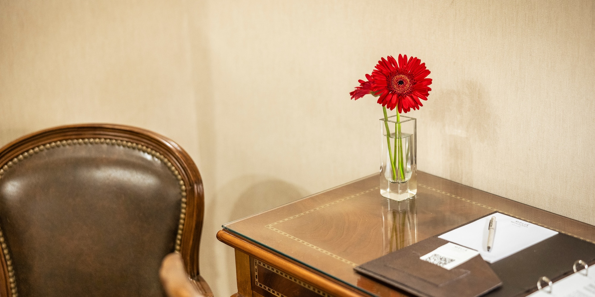 a red flower in a glass vase on a desk