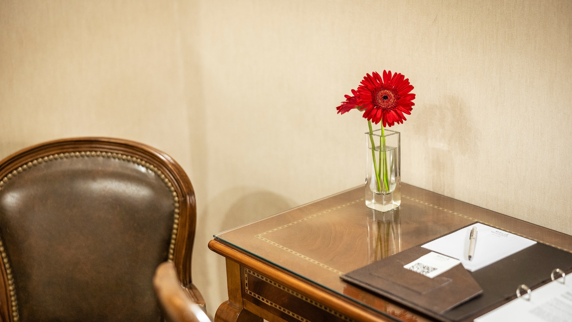 a red flower in a glass vase on a desk