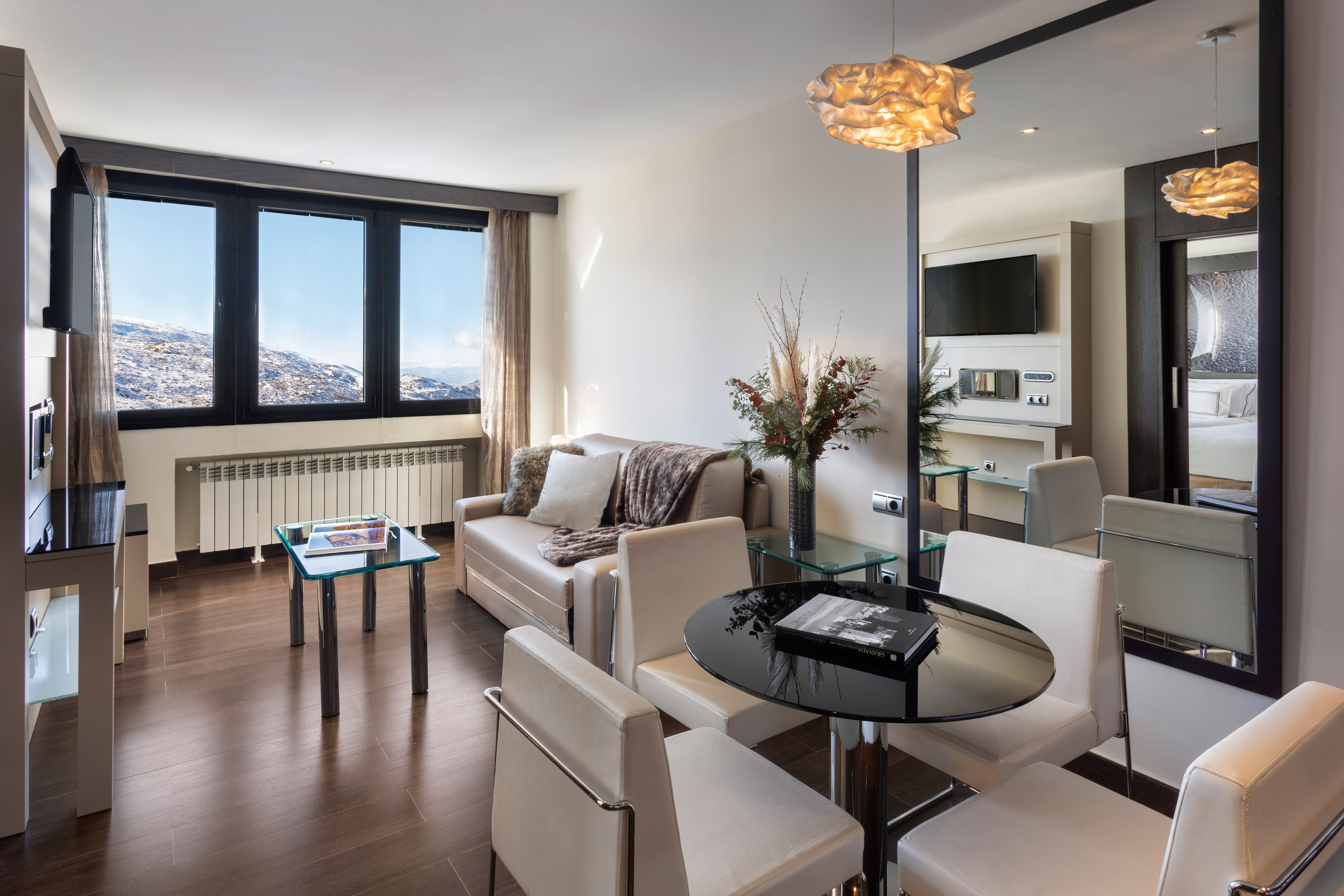 Modern ski resort living room with snowy mountain view, sofa, and dining area.