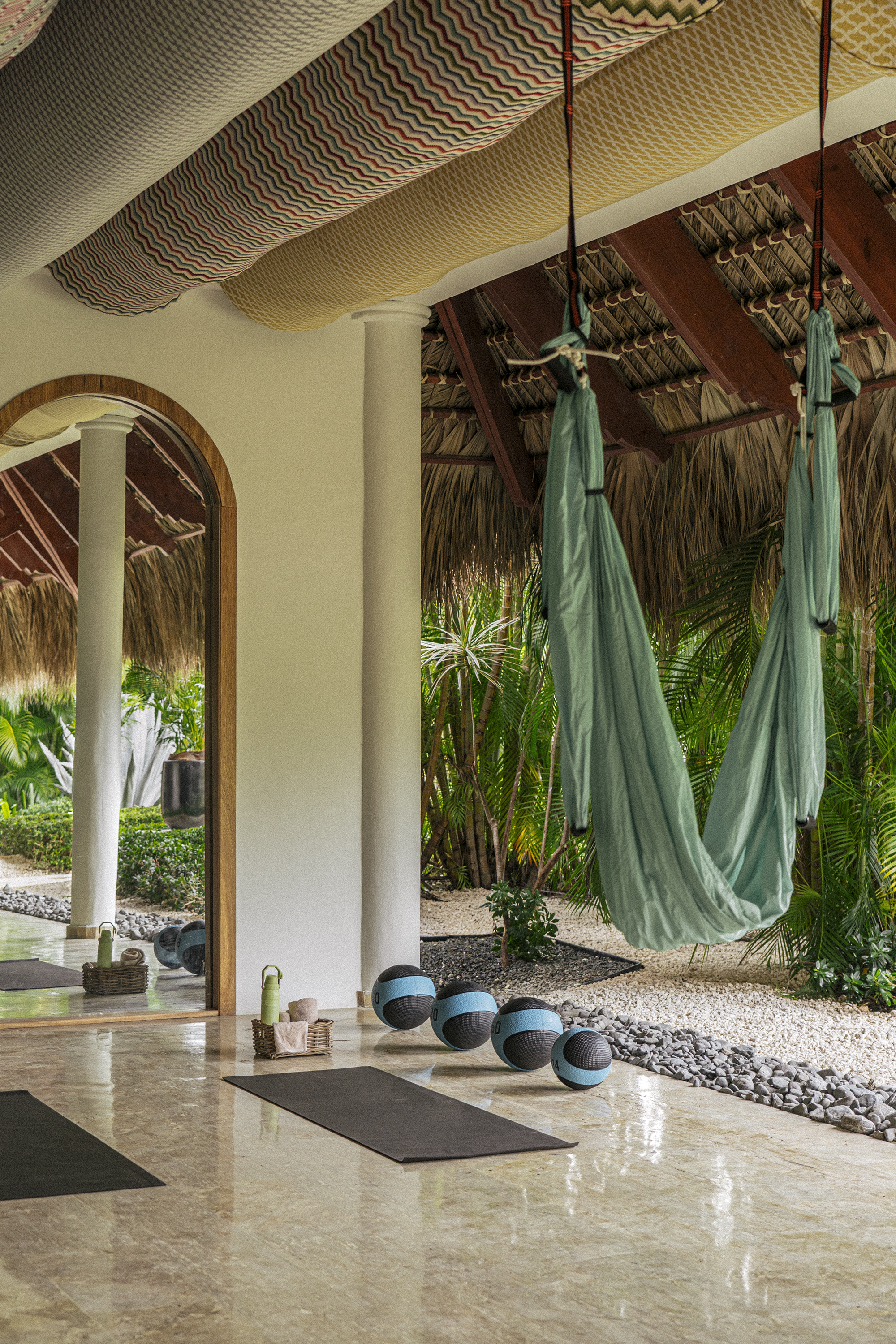Tropical outdoor yoga studio with aerial hammocks, mats, and medicine balls.