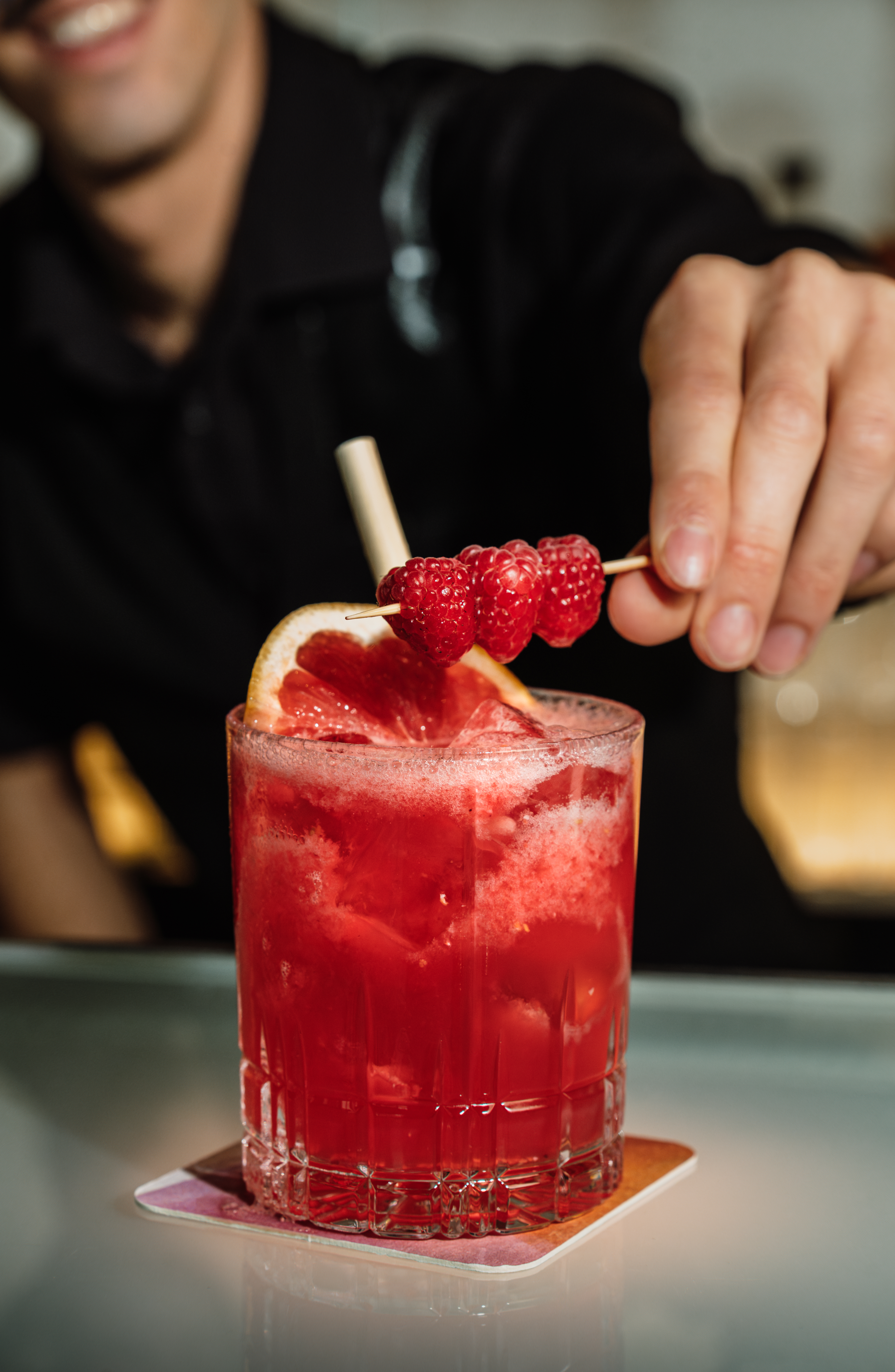 Bartender garnishing a red cocktail with raspberries and grapefruit.
