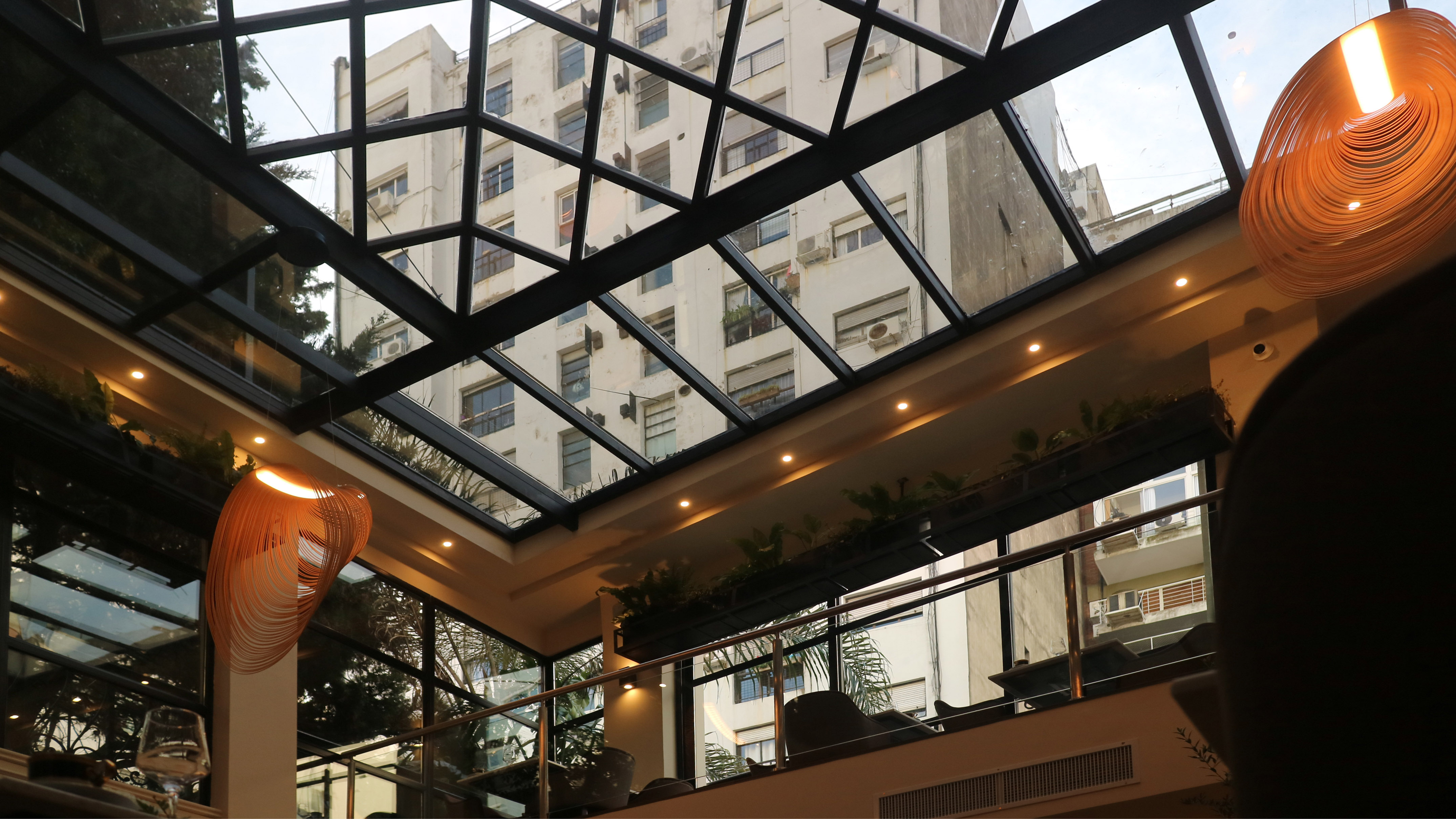 Modern restaurant with glass ceiling, urban building view, and spiral light.