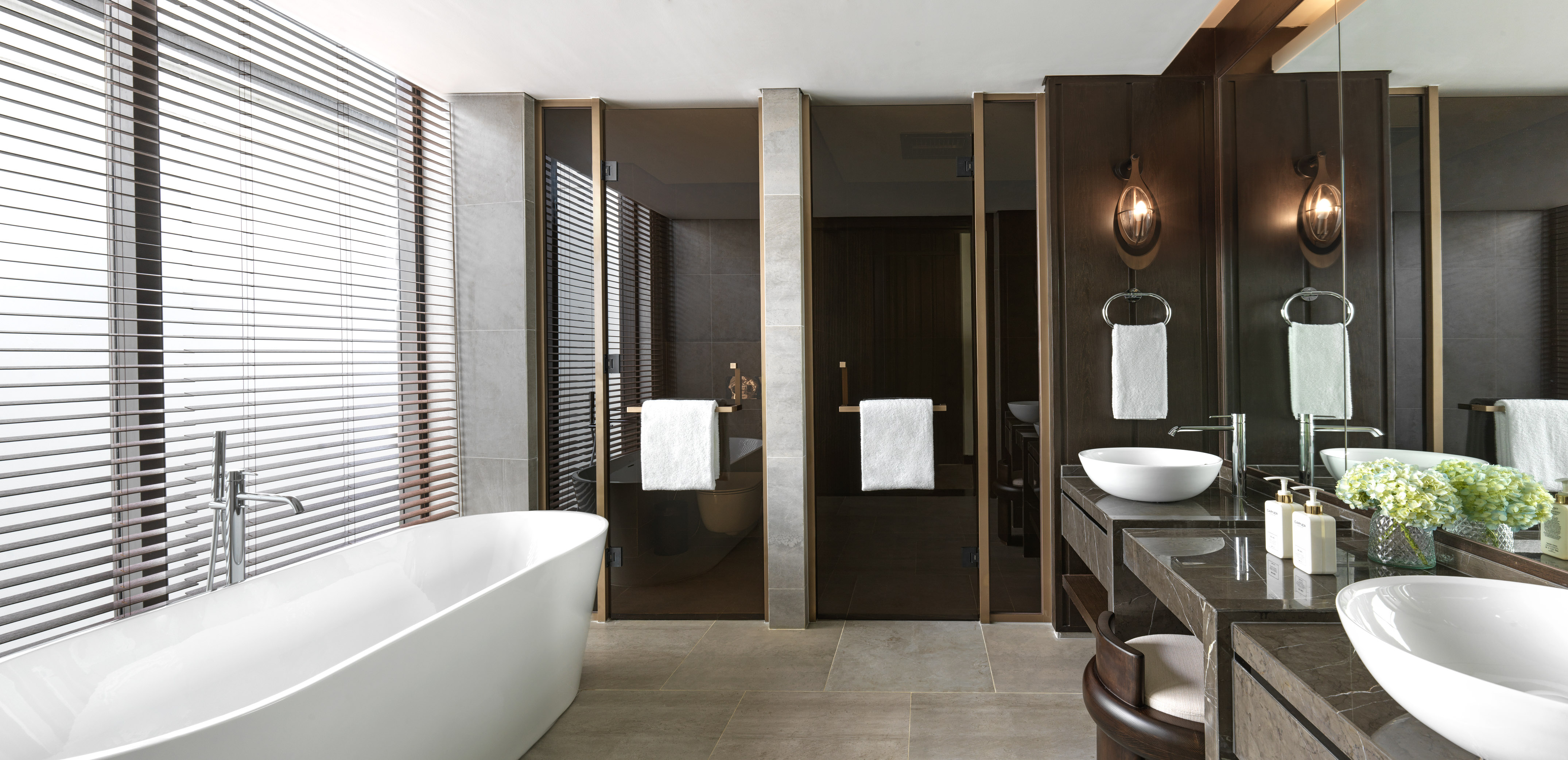 Modern luxury bathroom with freestanding tub, double vanity, and large window blinds.