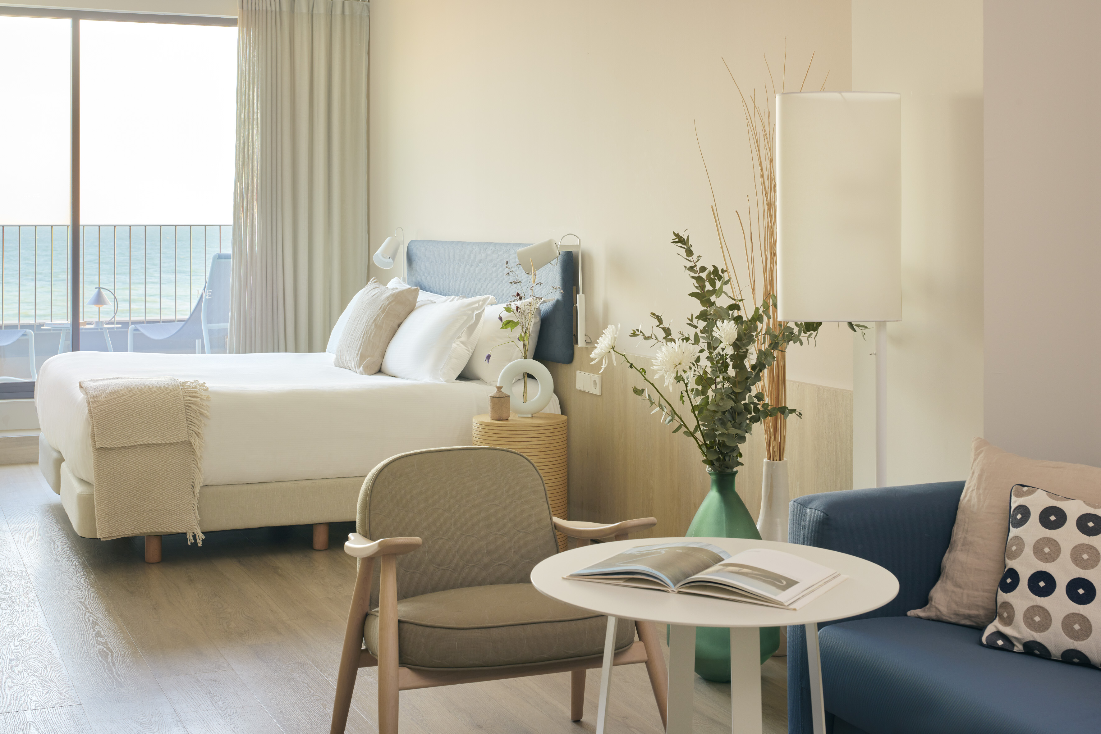 Modern hotel room with sea view balcony, white bed, and blue sofa.